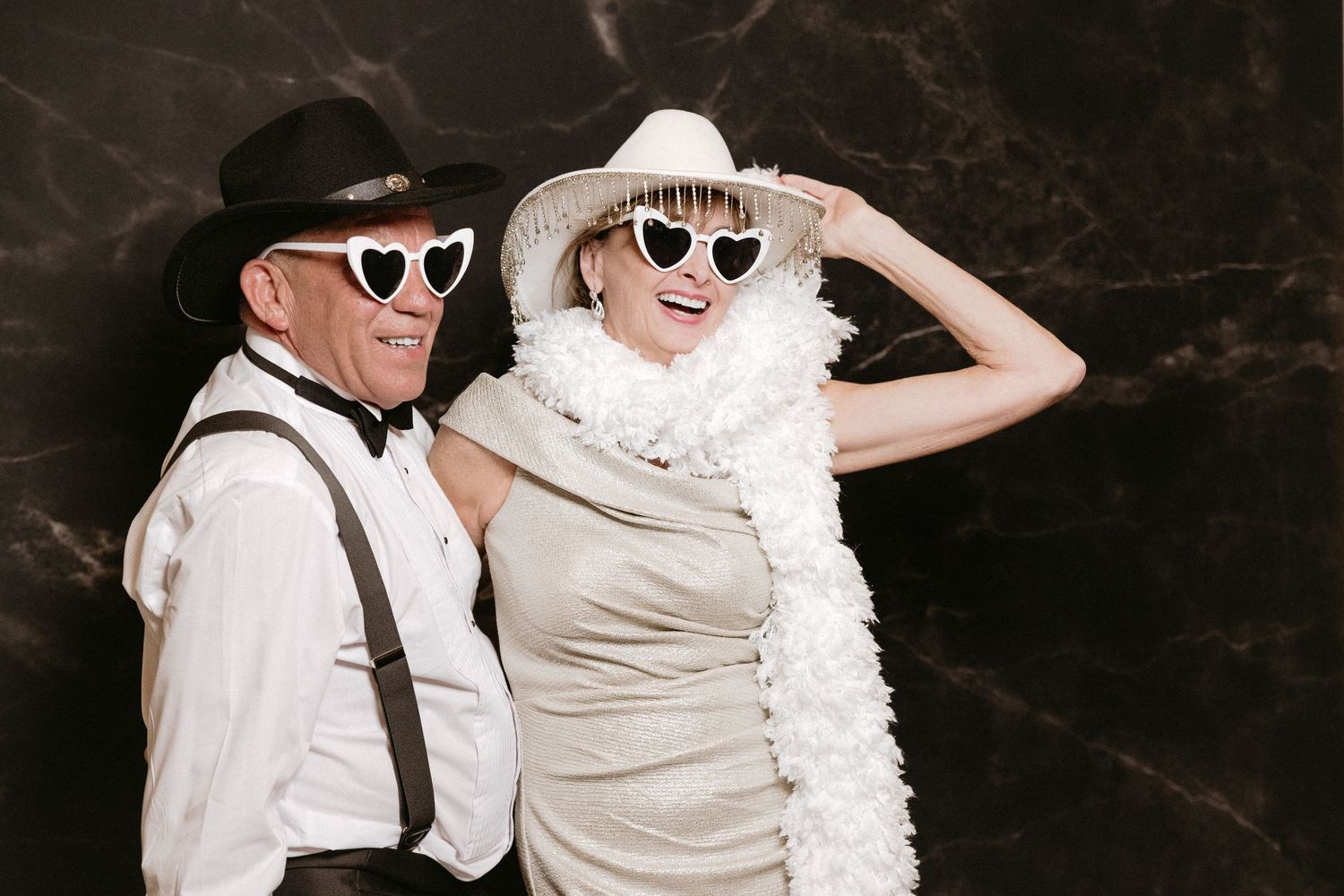 Two celebrants dancing together at a wedding reception, one in a flowing white dress and one in dark attire with a hat.