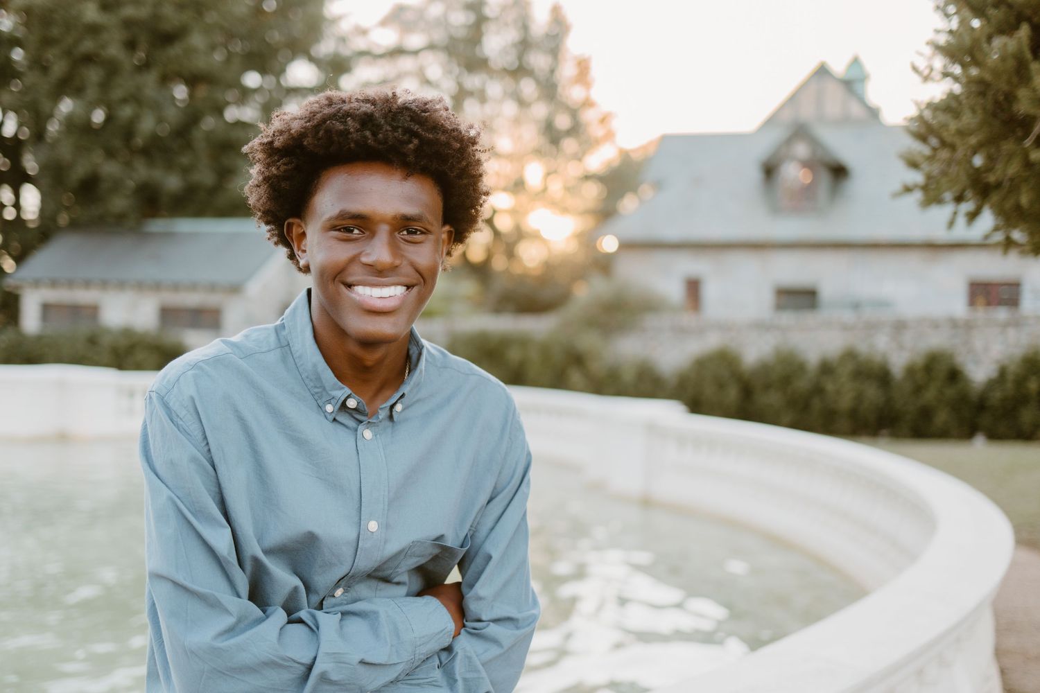 Person wearing light denim shirt and curly hair sits smiling outdoors during golden hour at sunset.