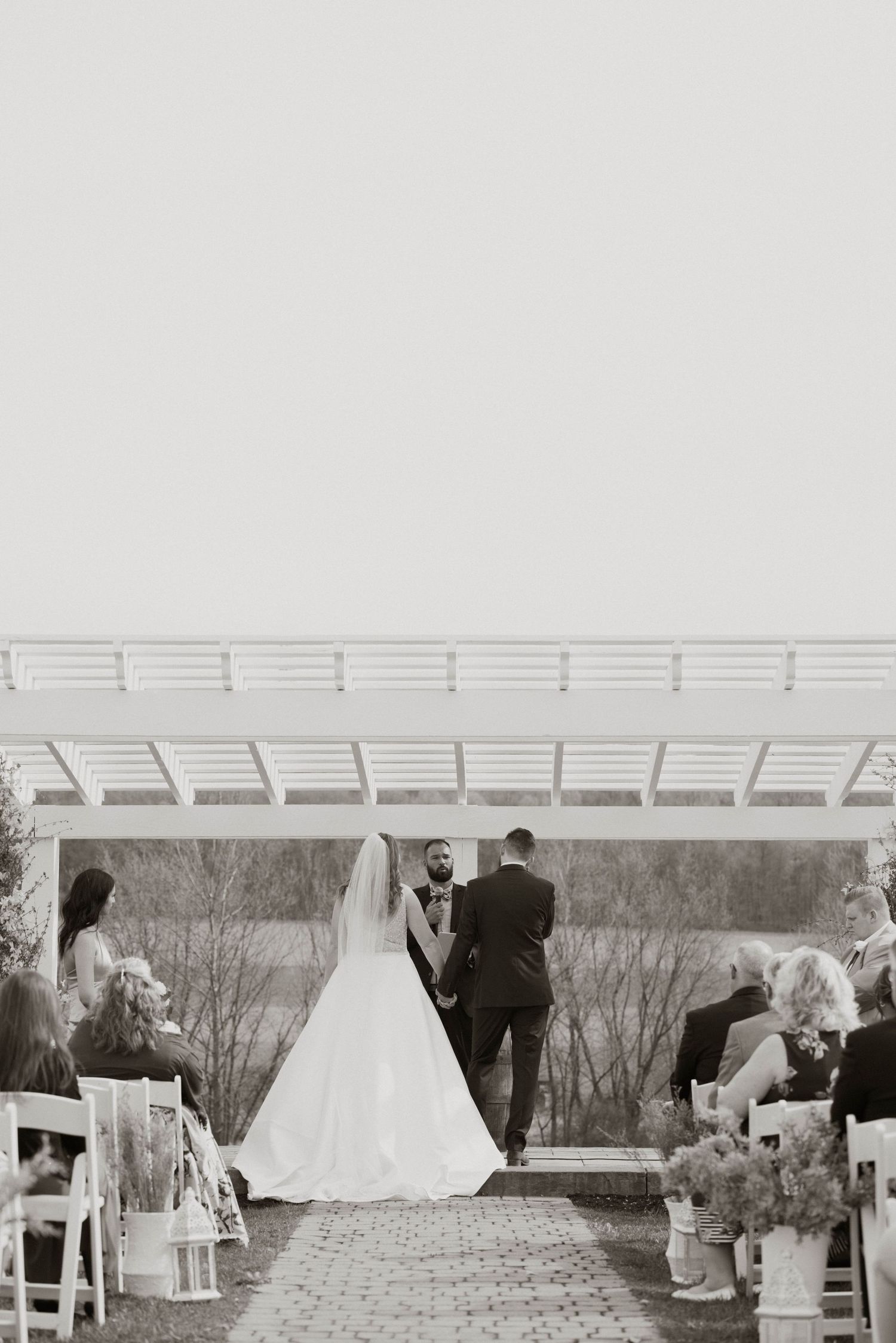 Black and white photo of outdoor wedding ceremony setup with white pergola and chairs.