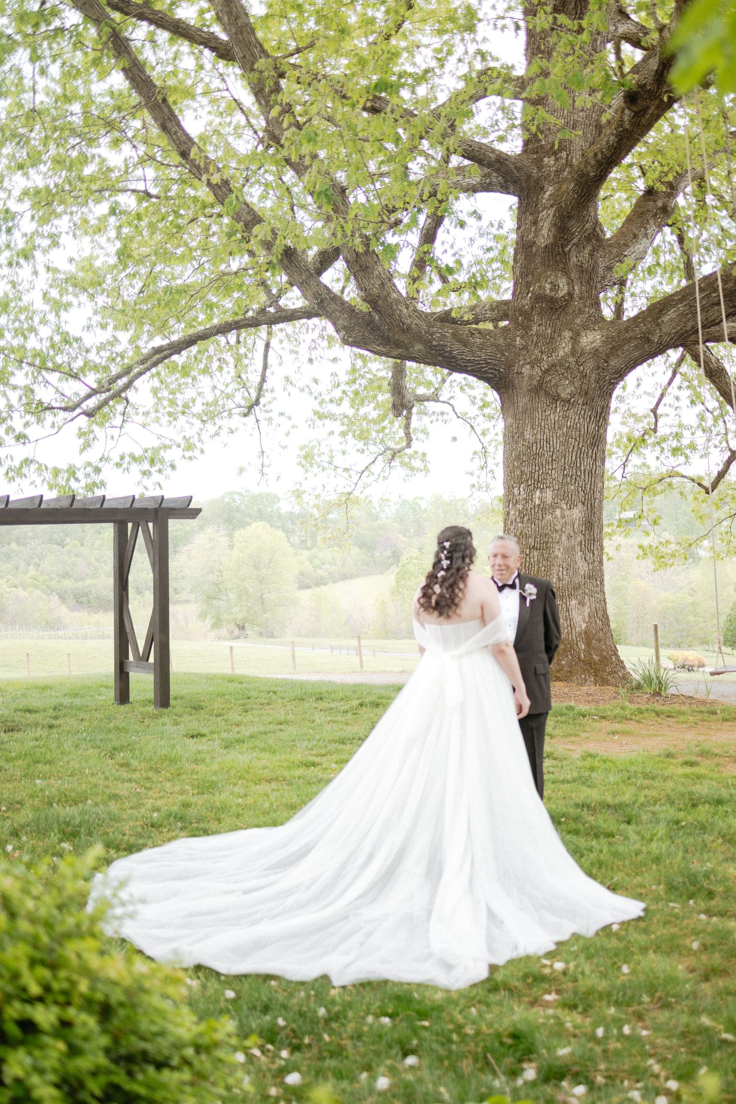 Wedding couple embraces under blooming trees with a flowing white dress trailing on the grass.