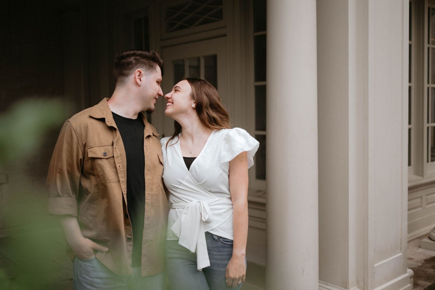 A couple shares intimate kisses in front of a white column, captured in a romantic lifestyle photography shoot.