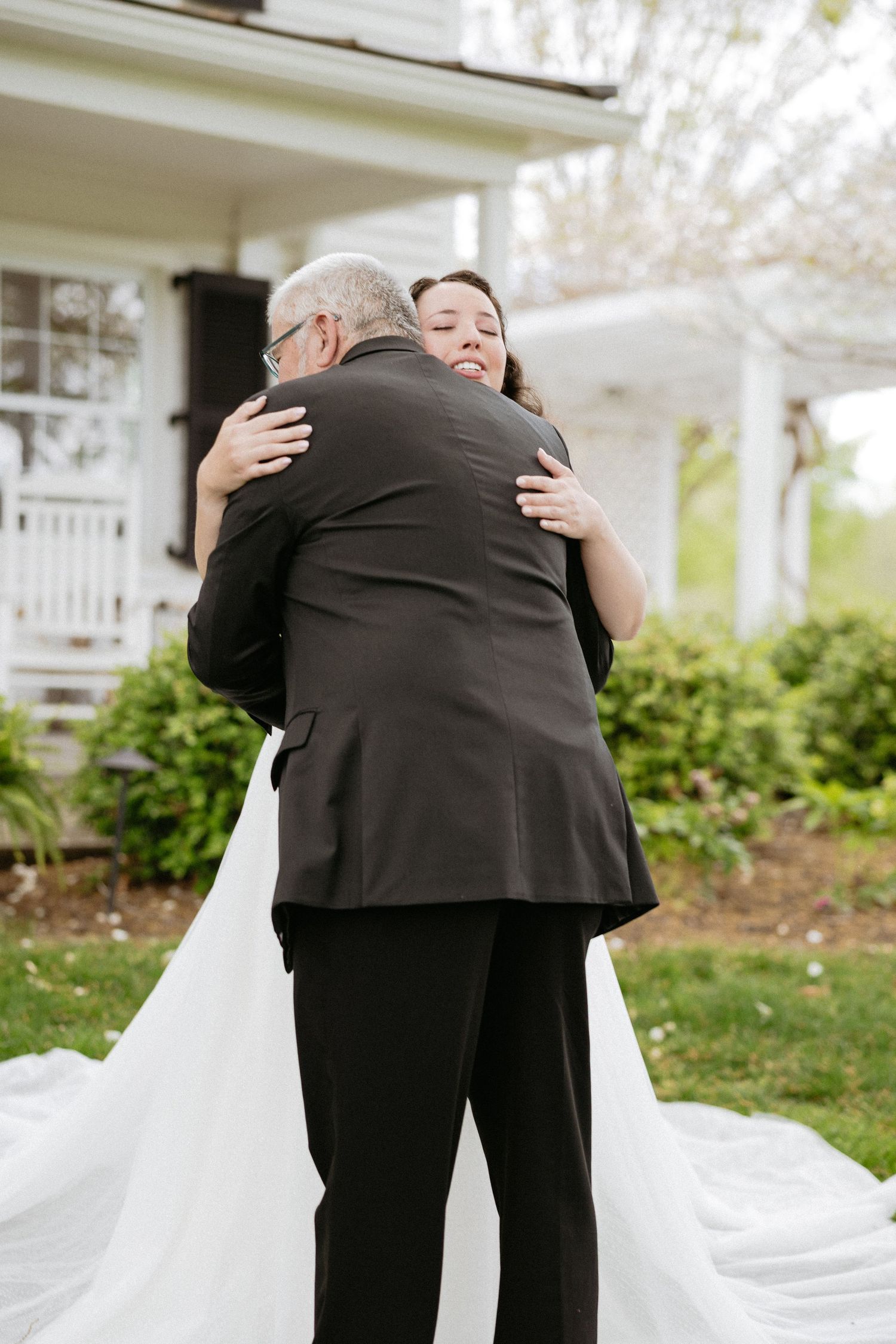 Heartwarming embrace between wedding couple in formal attire against white building exterior.