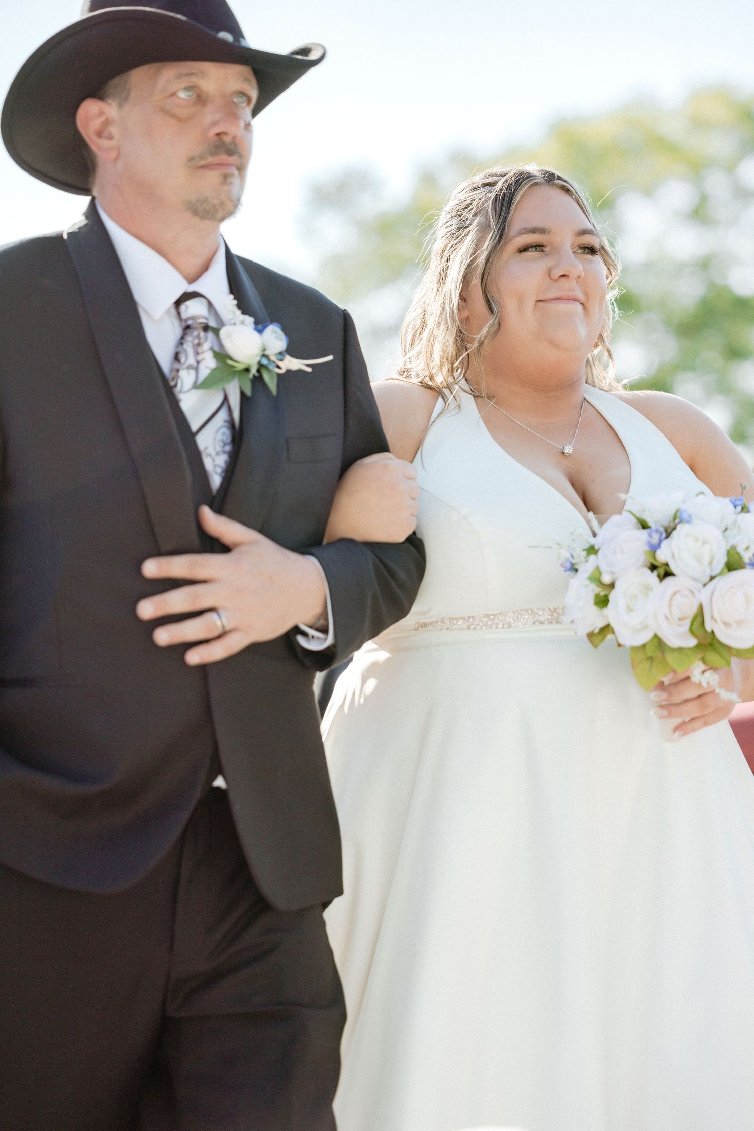 A couple in formal wedding attire photographed with sunlight and blossoms in the background.