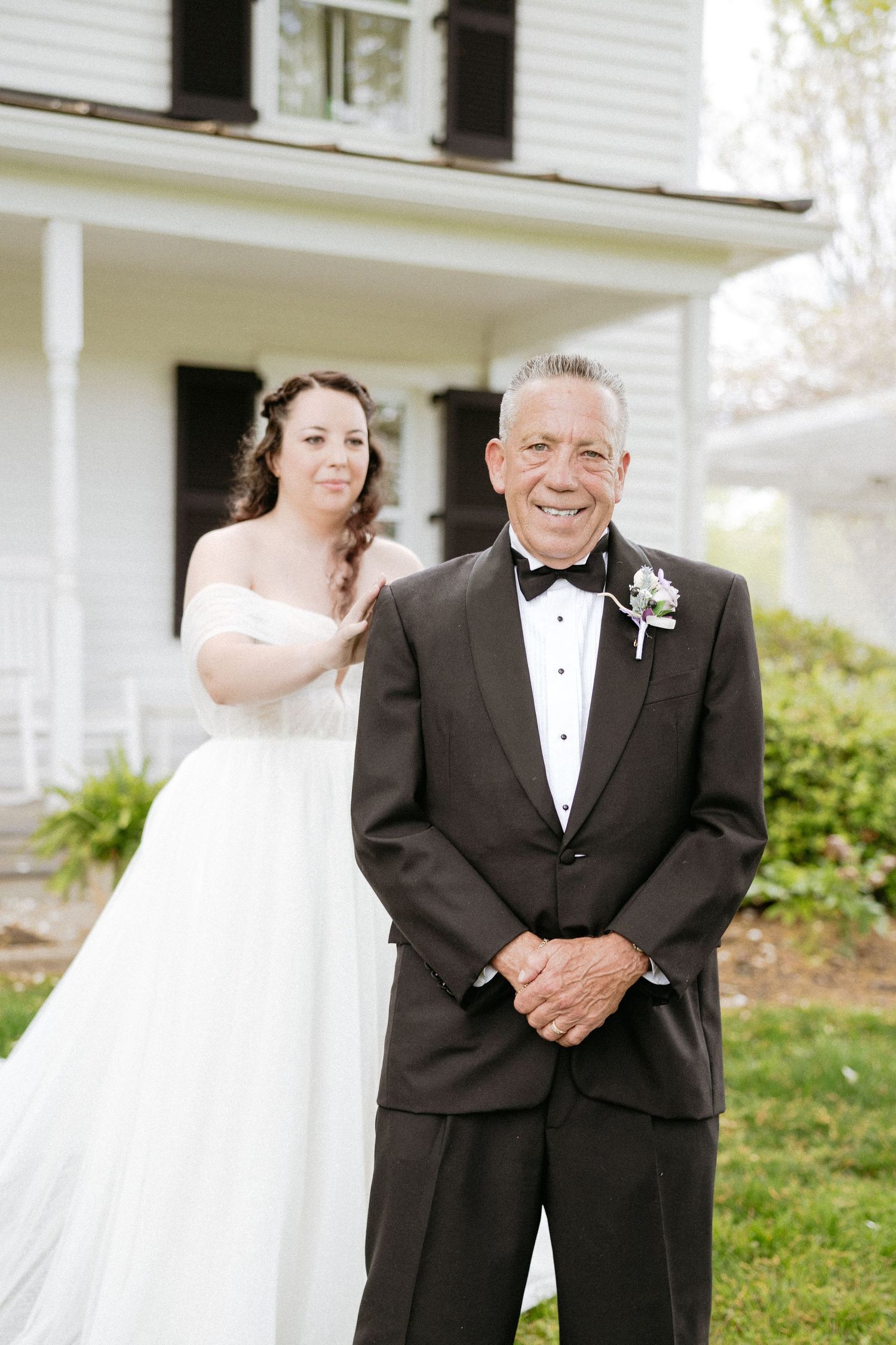 Emotional first look sequence between bride in white gown and companion in black tuxedo outside white porch.