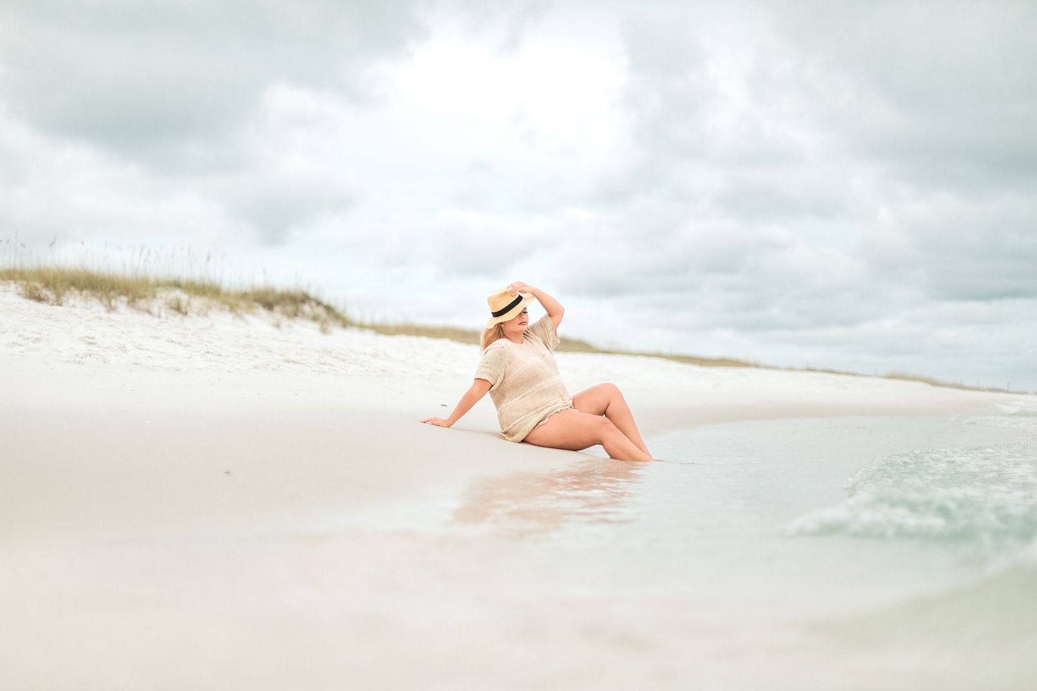 A serene beachside scene with a figure in pink swimwear relaxing at the water's edge on white sandy shores.