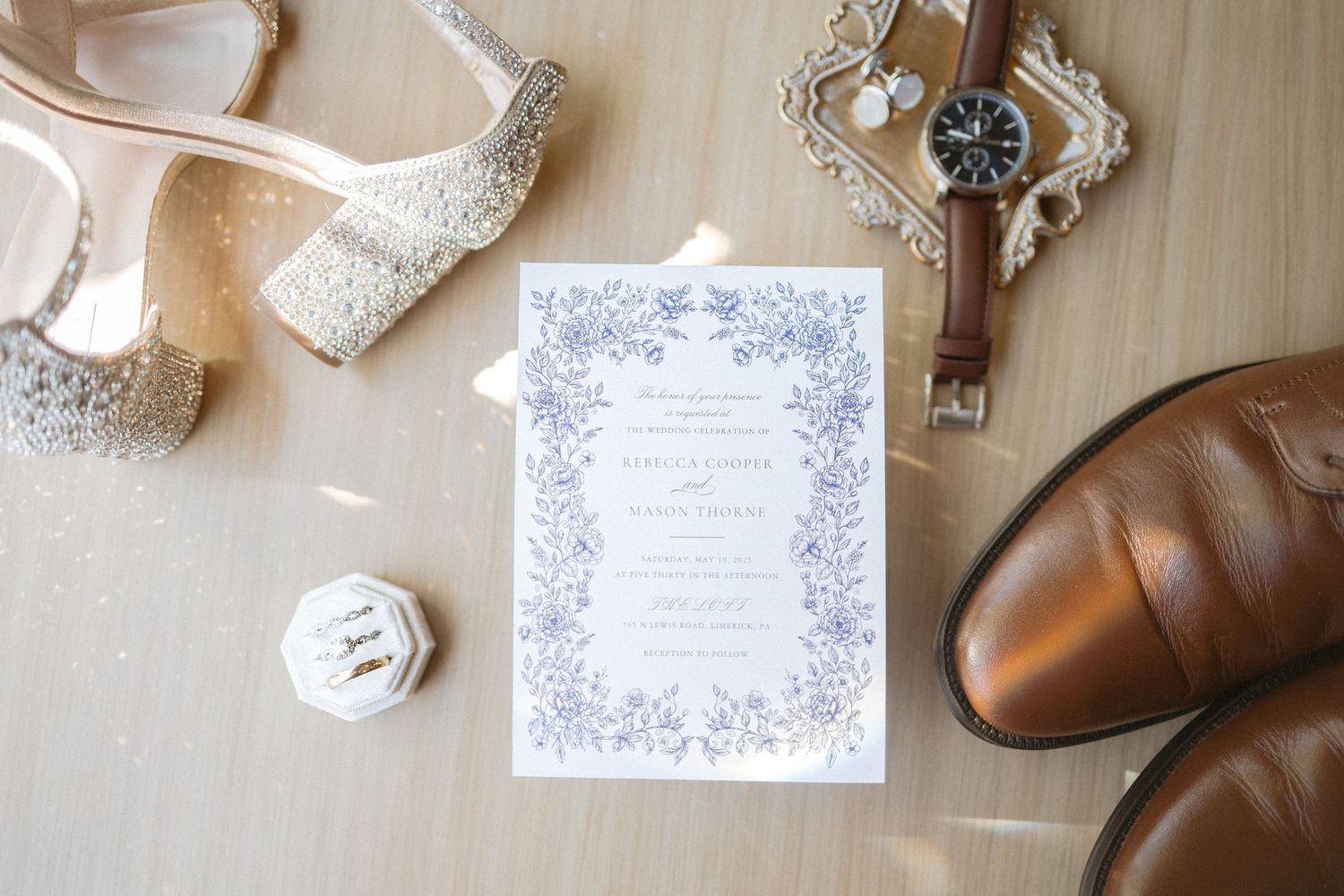 Wedding accessories including white lace shoes, dress details, and brown leather dress shoes displayed on wooden surface.