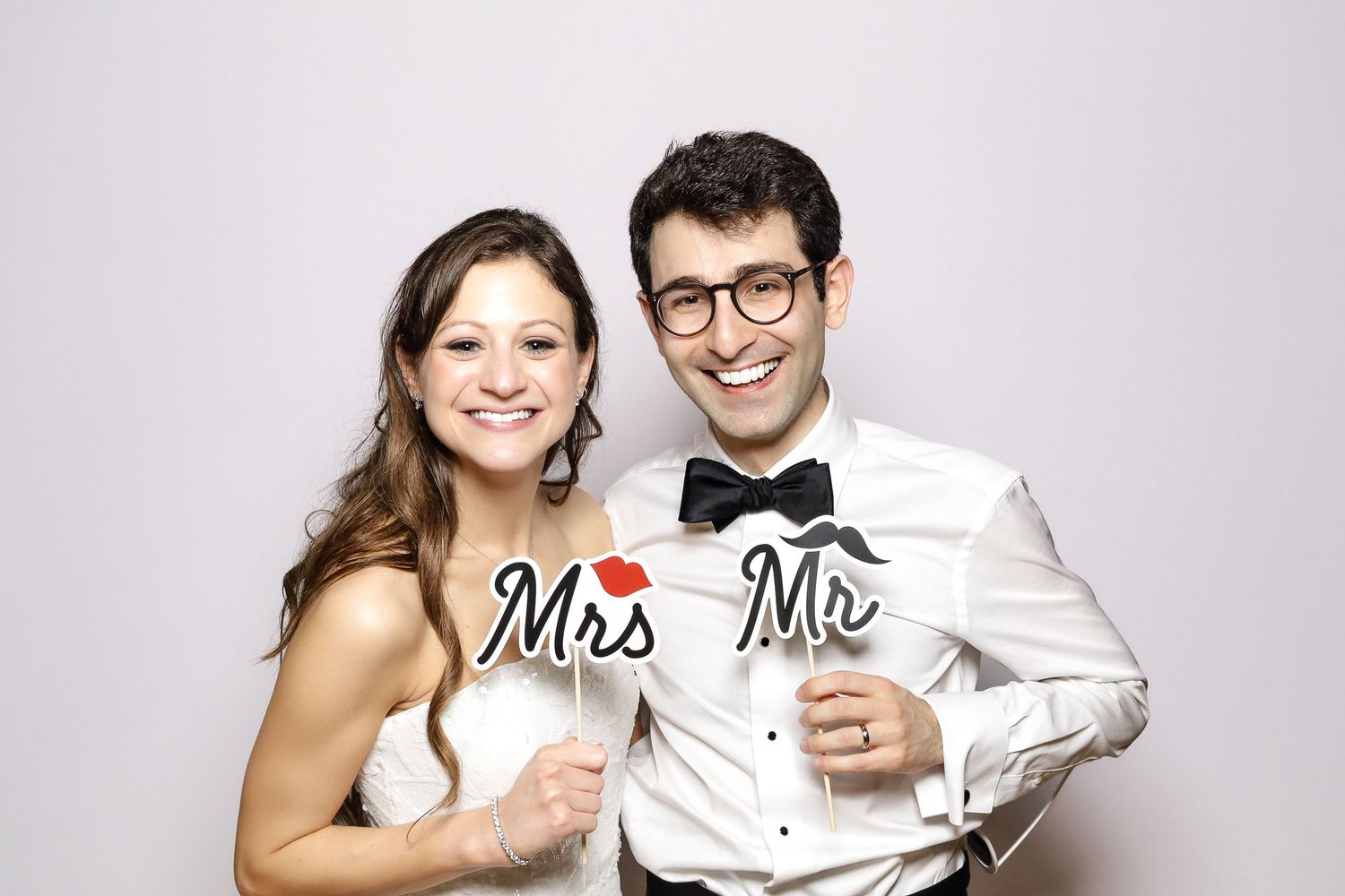 A wedding photo booth portrait of a couple holding Mr and Mrs signs while smiling at the camera.