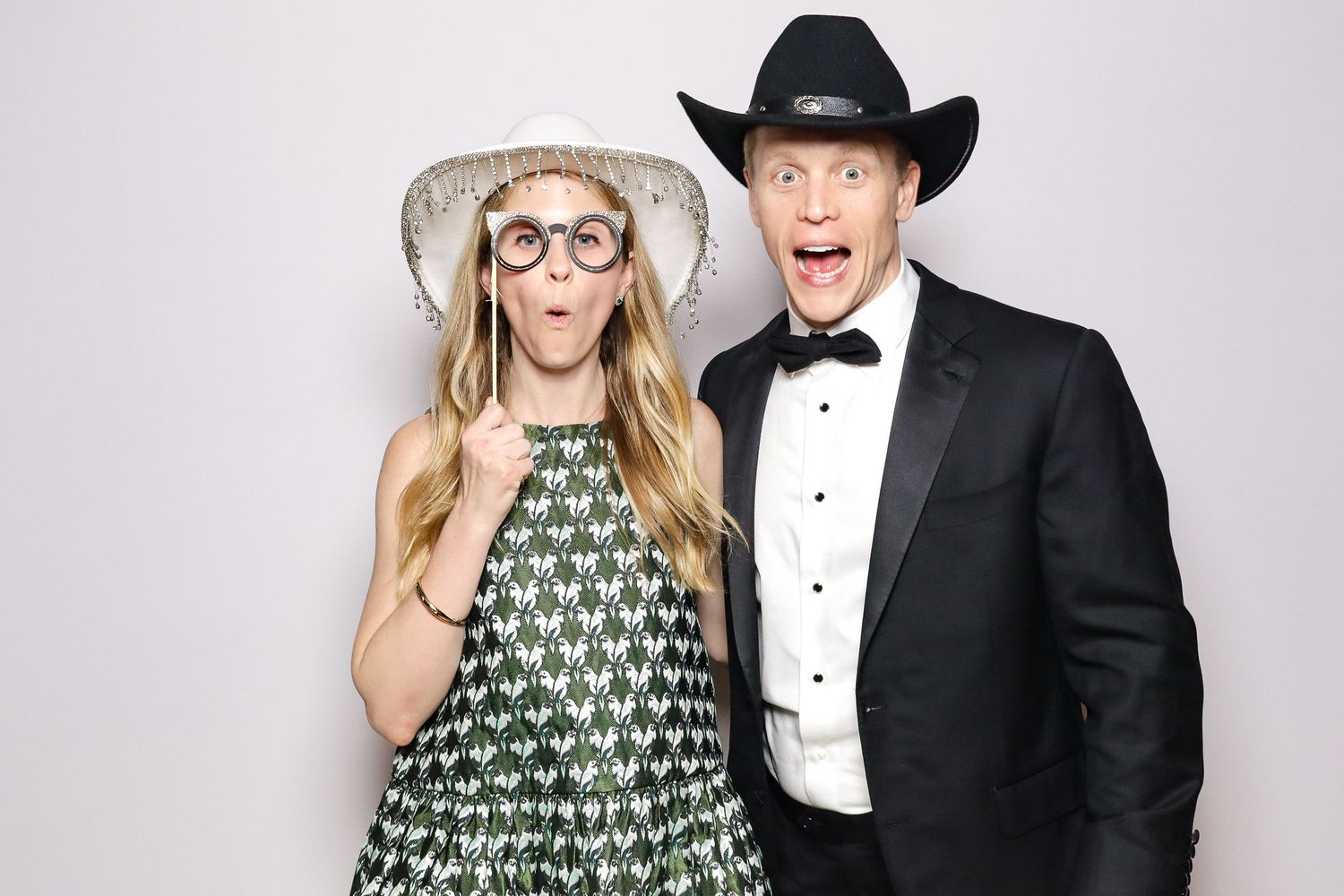A playful photo booth shot of two people in formal wear with one wearing a cowboy hat making surprised expressions.