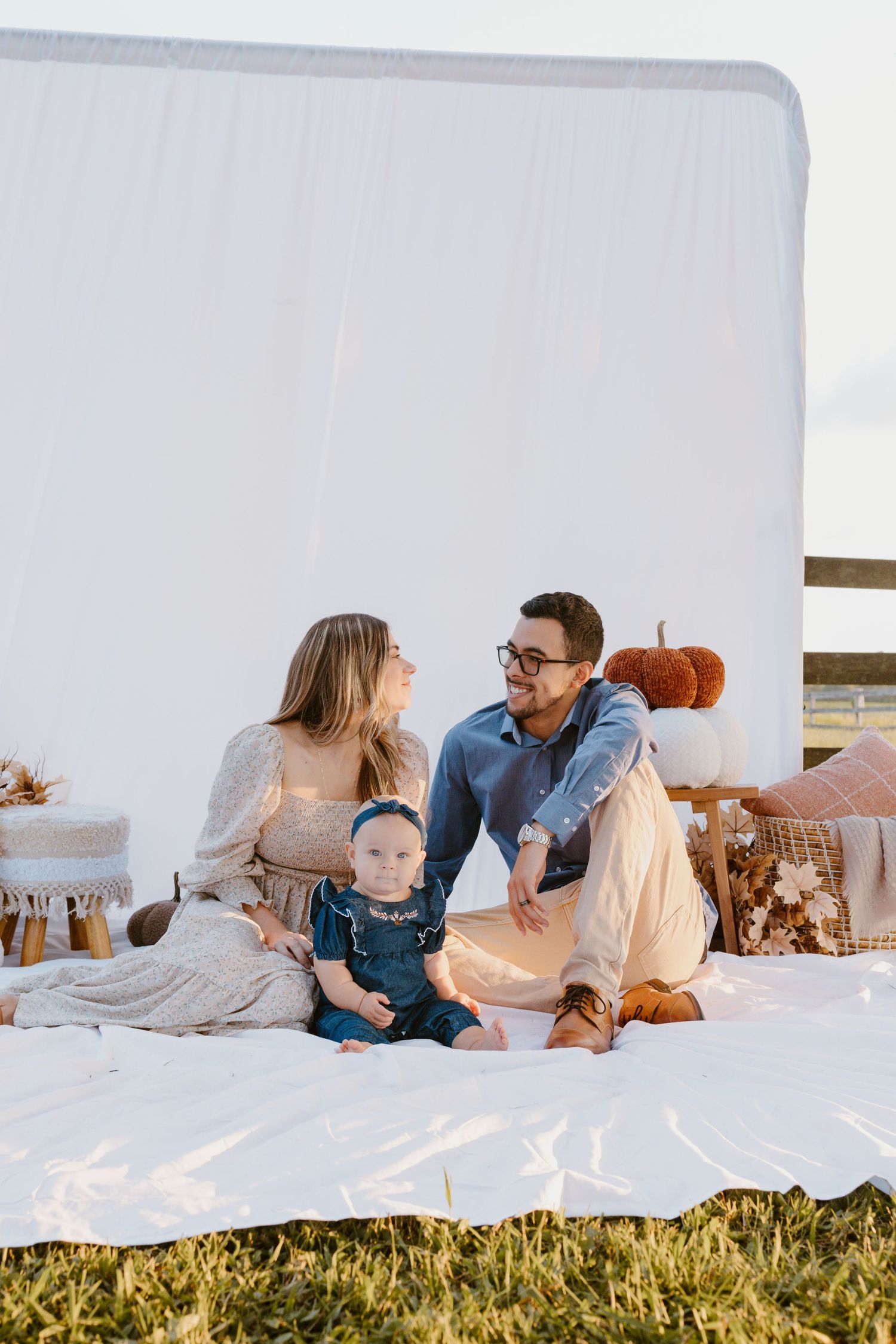 A family shares a tender moment together while relaxing on a white bed against a sunny outdoor background.