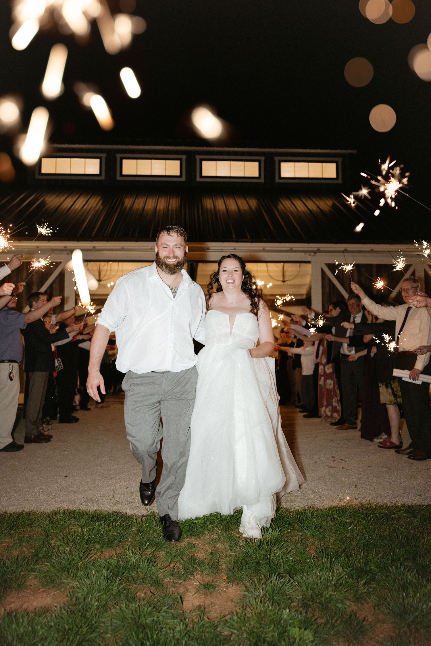 A nighttime wedding exit with sparklers lighting up the path as newlyweds walk through under string lights.