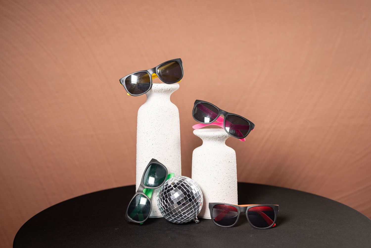 Colorful sunglasses collection displayed with white decorative items and silver disco ball.