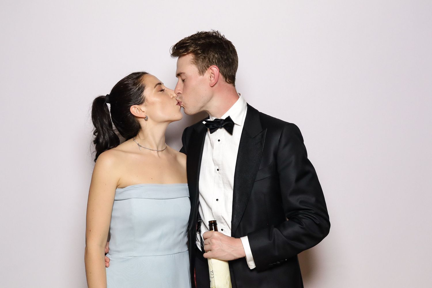 A romantic photo booth moment capturing a couple in formal wear sharing a kiss.