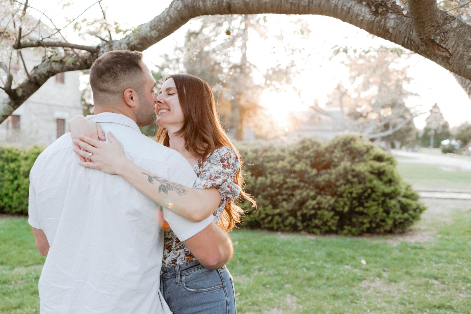 A couple shares three tender embraces while standing outdoors during a countryside lifestyle photoshoot at sunset.