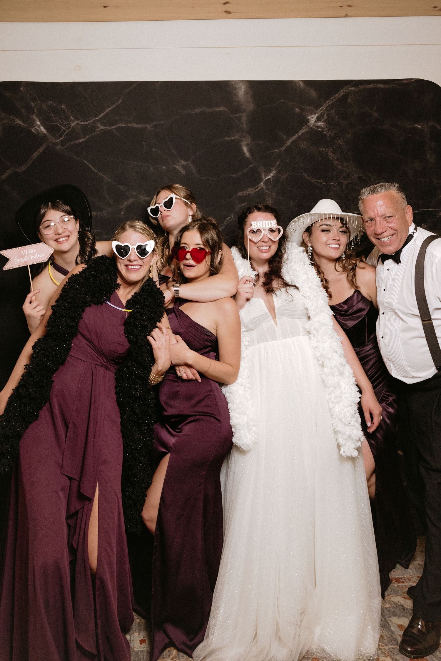 Wedding party wearing sunglasses and burgundy dresses poses playfully for group photos.
