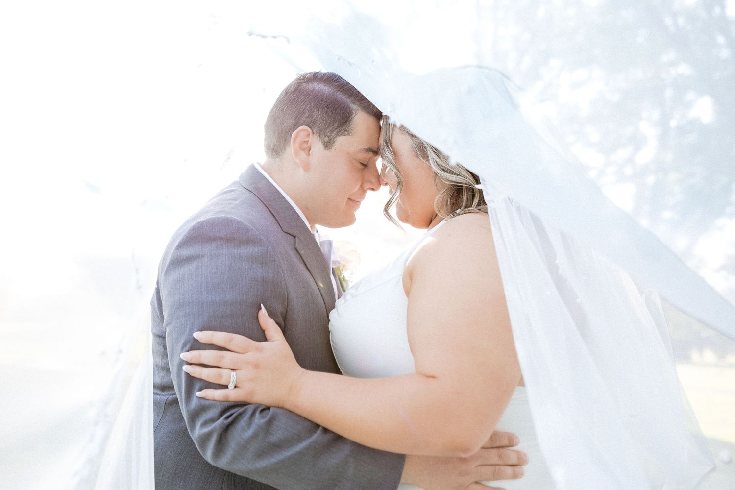 A loving couple shares a tender embrace during their outdoor wedding ceremony on a bright sunny day.