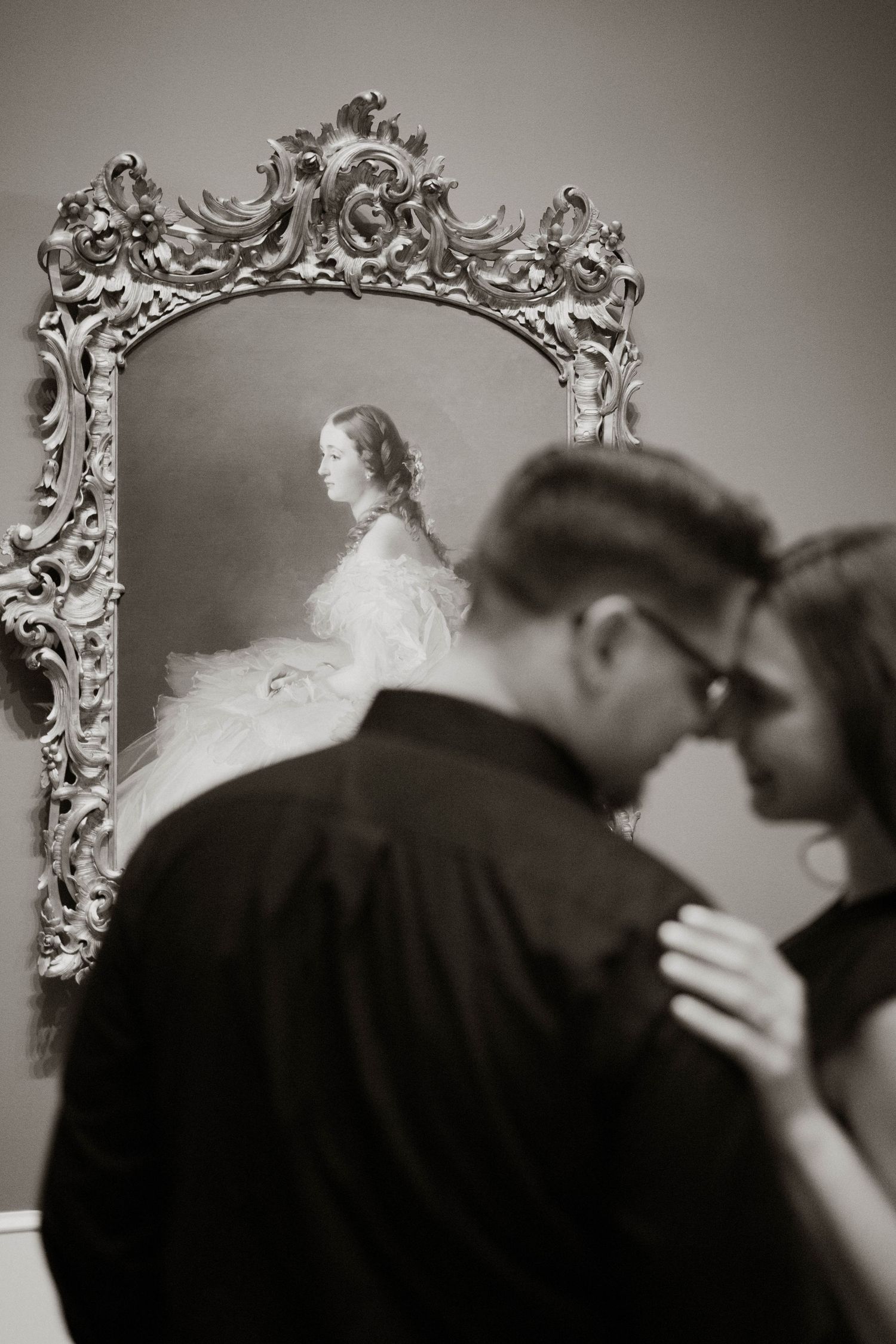 Vintage-style black and white photography showing a romantic couple in an ornate frame mirror reflection.