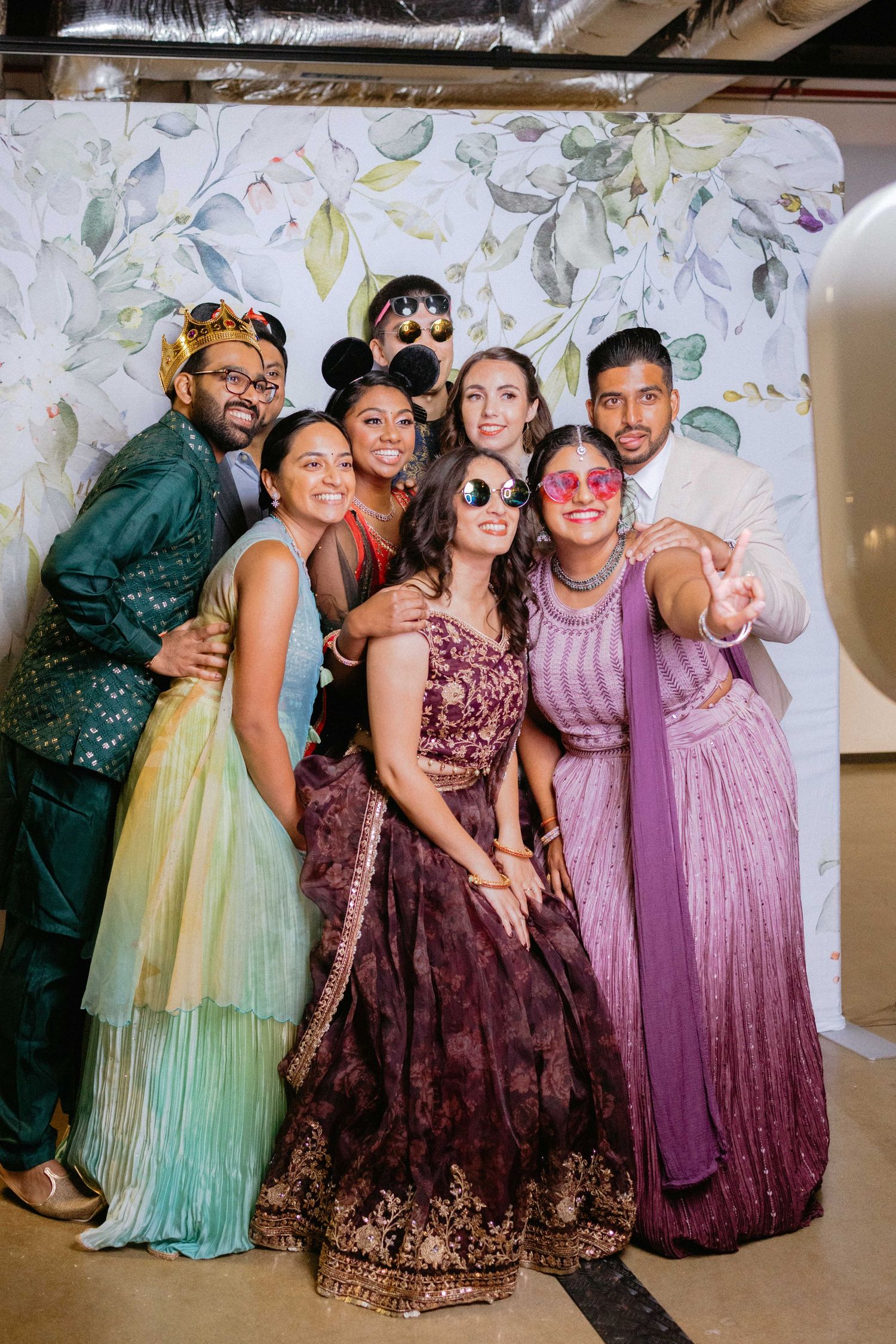 Wedding party in colorful formal attire poses together against a floral backdrop.