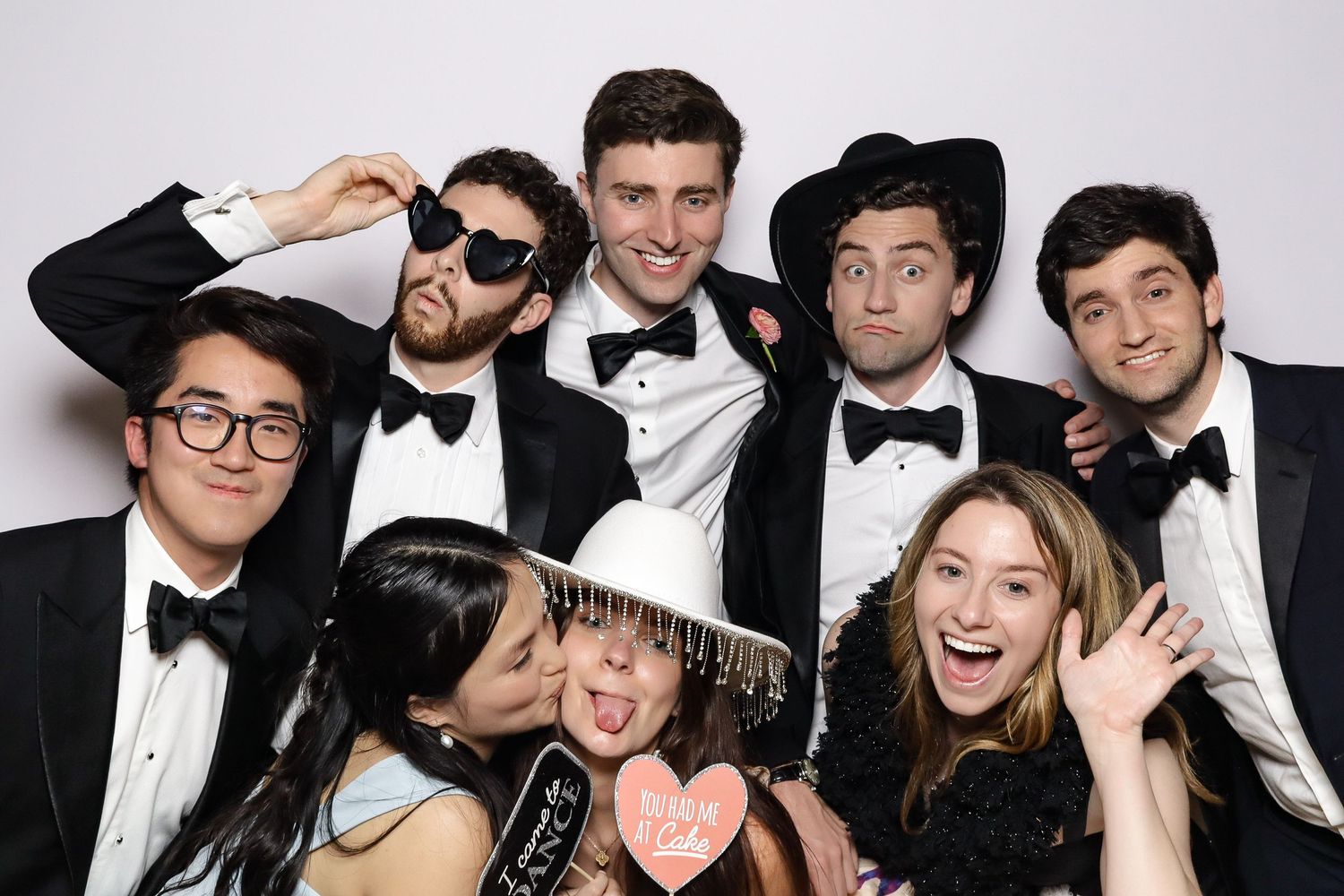 A fun photo booth shot of a wedding party in formal attire making silly poses with props.