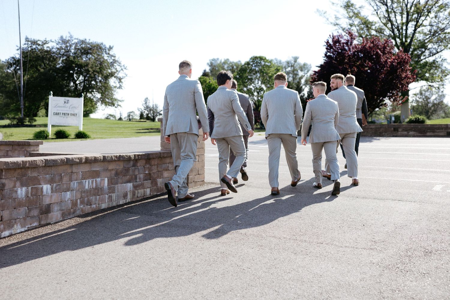 Wedding party walking together on a stone path outside with trees and bushes in background.