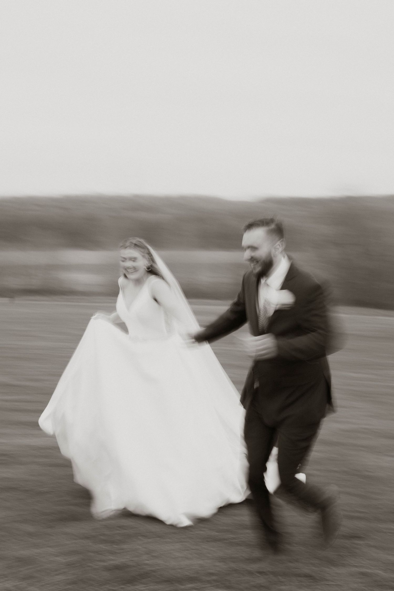 Black and white motion blur photos capture playful moments between wedding couple on grassy field.