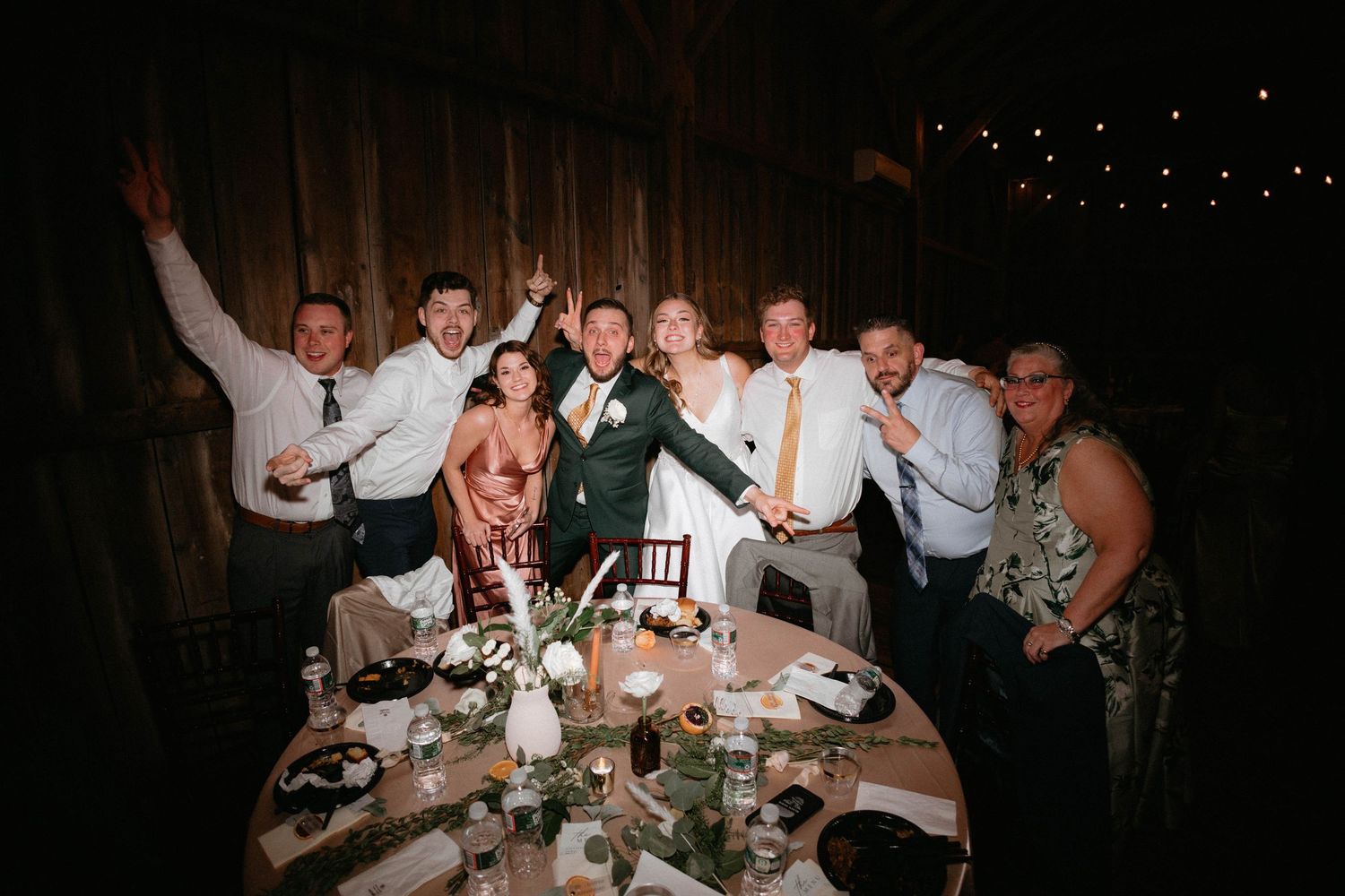 Wedding reception guests gather at long tables under string lights during an elegant evening celebration.