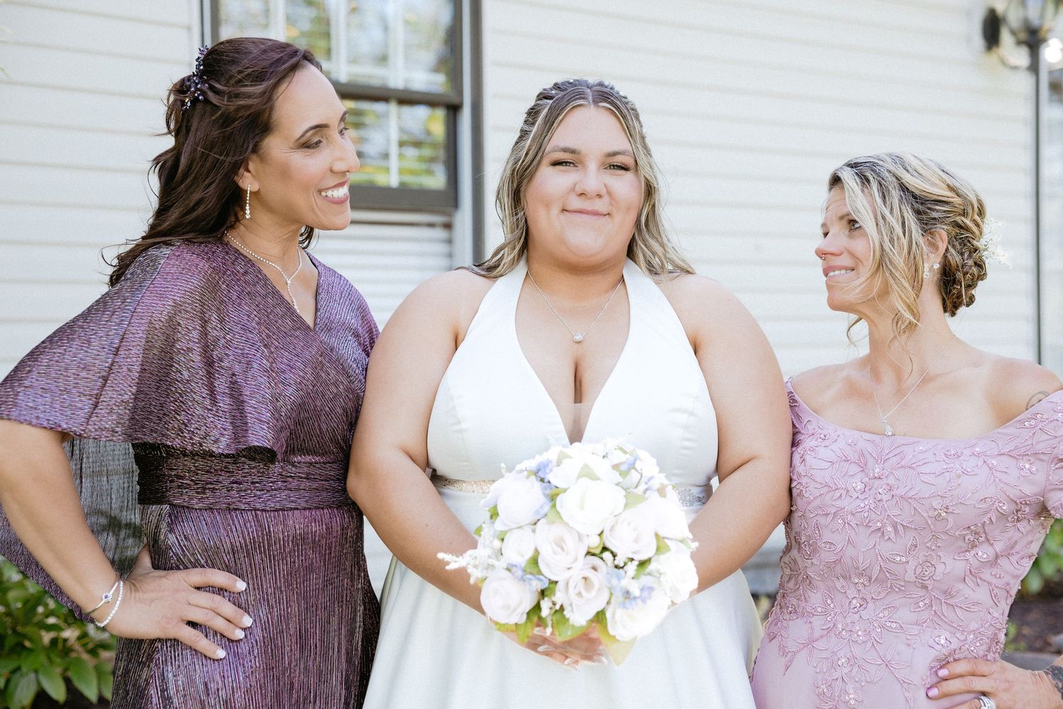 Wedding party in coordinated purple and mauve dresses poses together for formal portraits.