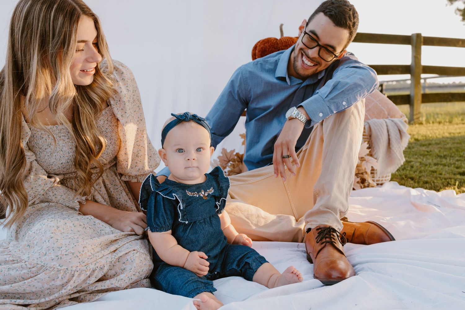 Family lying on white blanket outdoors during sunset with golden light creating warm atmosphere.