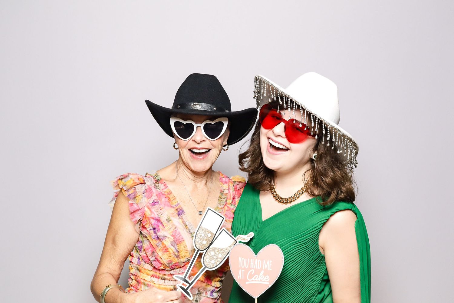 Two people in cowboy hats and sunglasses pose with heart props in a festive photo booth shot.