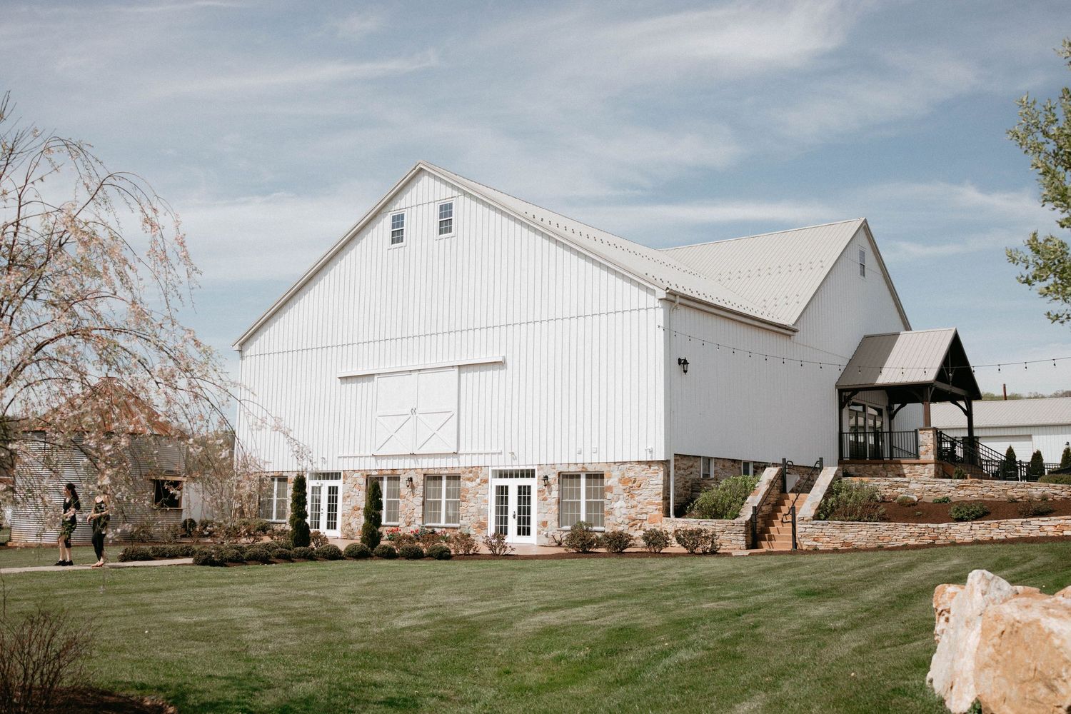 Modern white barn wedding venue with well-maintained lawn and rustic architectural details stands against blue sky.