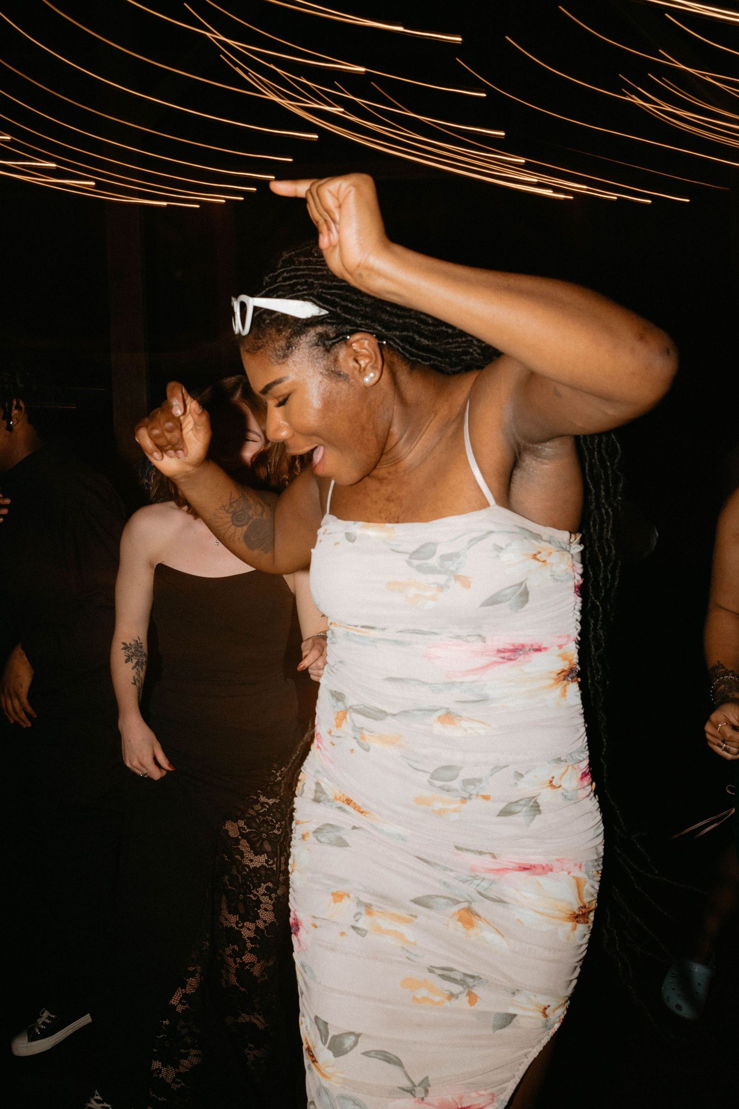 Wedding guests dancing and celebrating on dark dance floor with festive lighting overhead.
