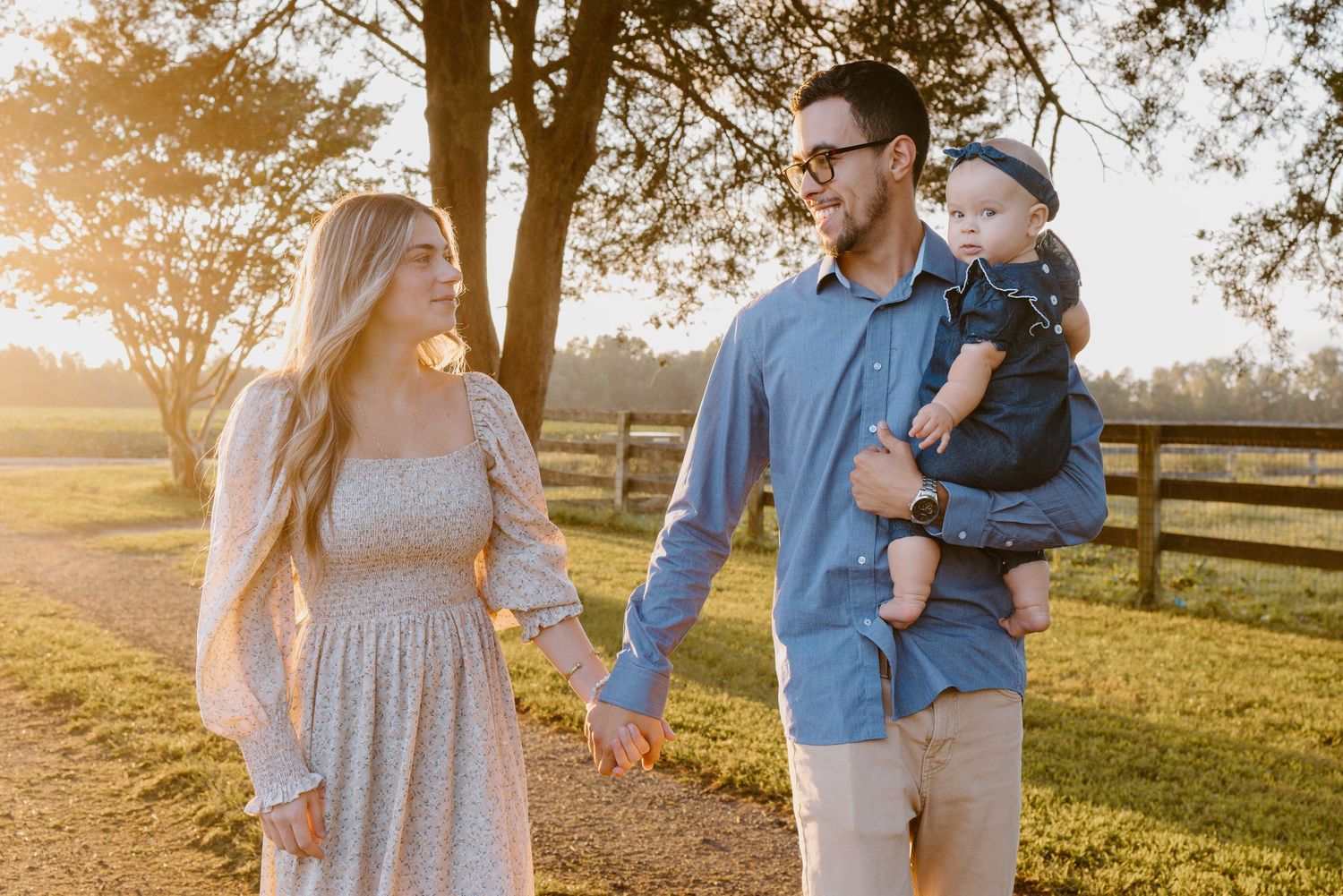 A couple in matching blue and gray outfits walking along a wooden fence during golden hour sunset.