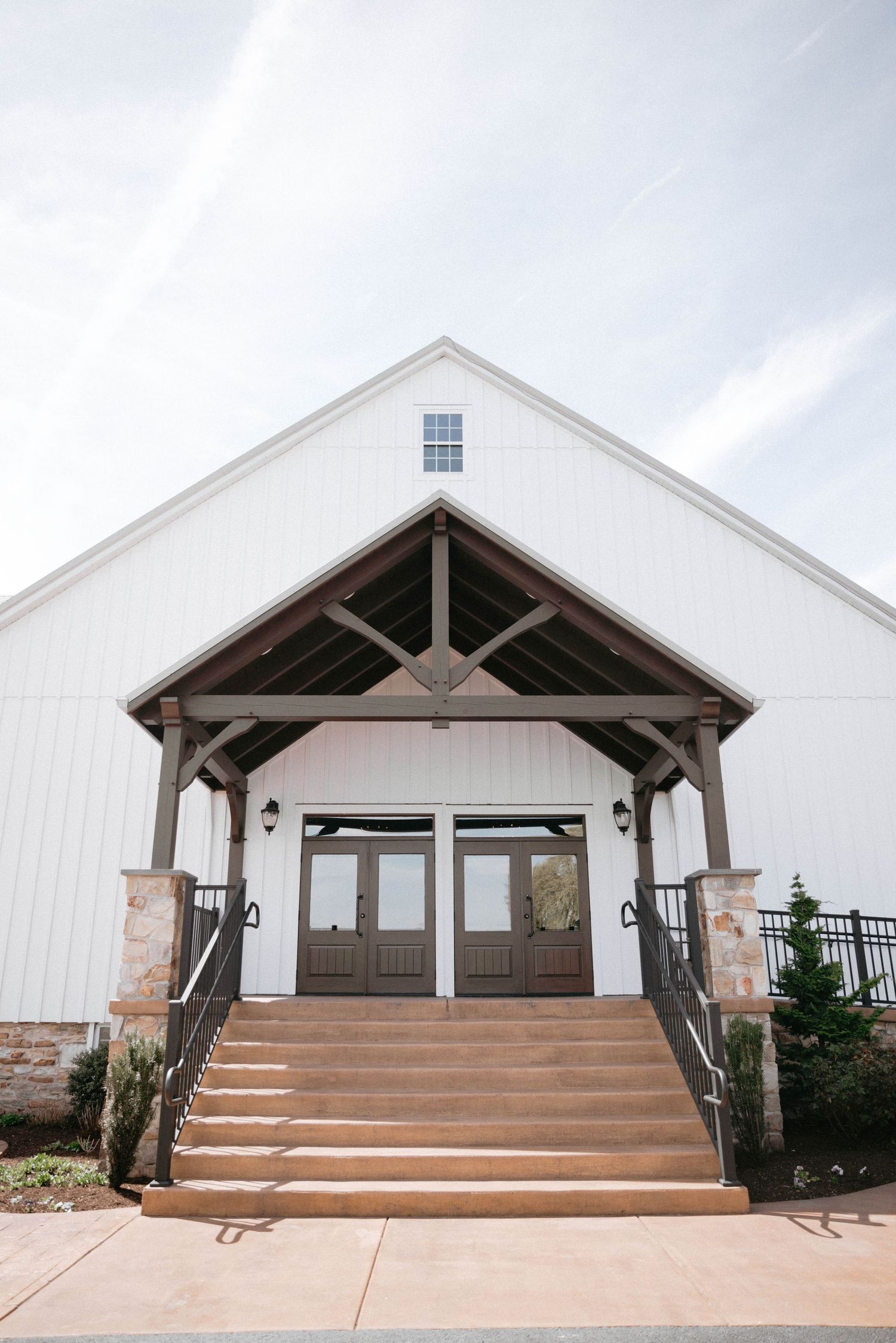 Modern white barn-style wedding venue entrance with wooden beams and stone accents.