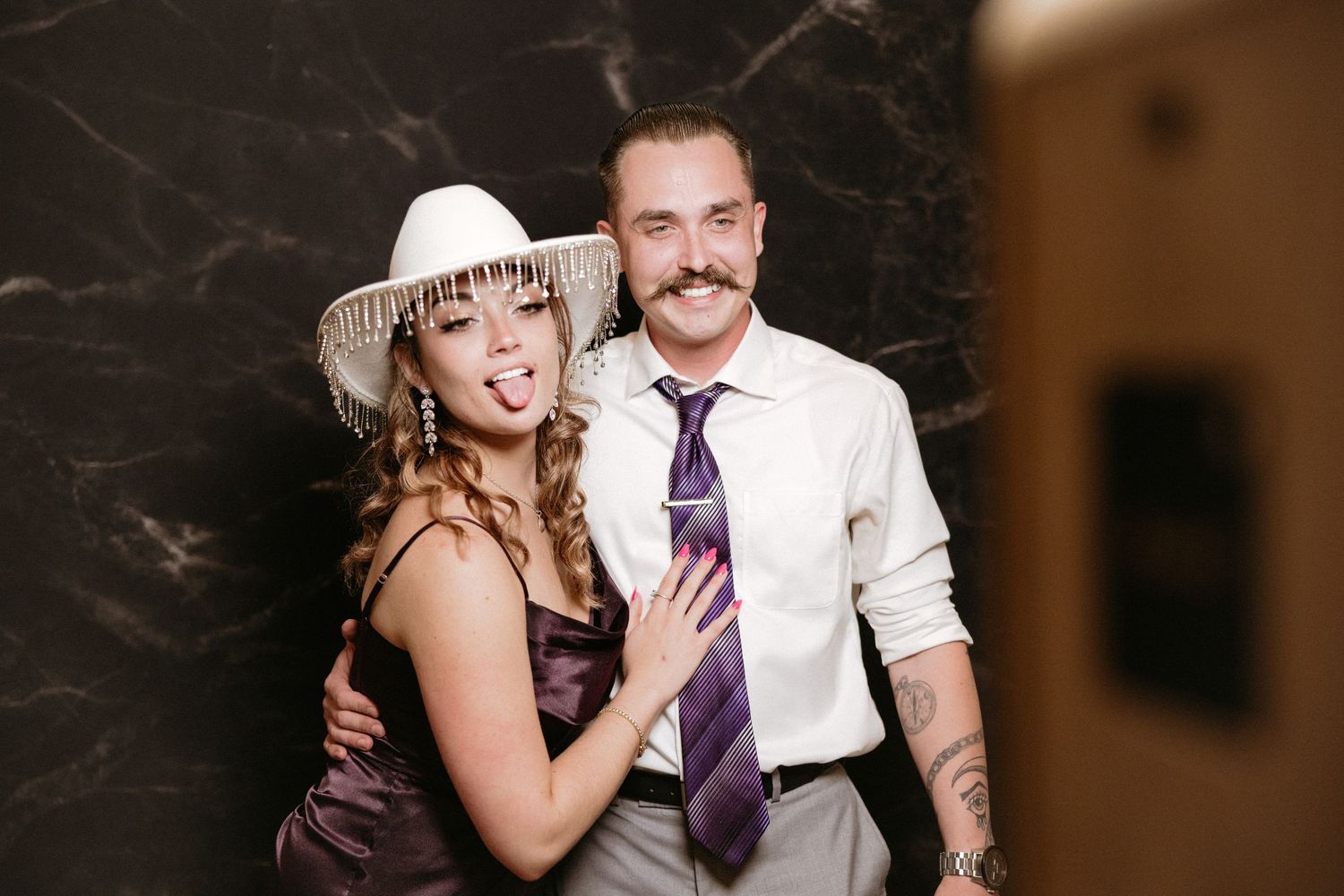 A photo strip sequence showing a couple posing playfully in formal attire at a vintage-style photo booth.