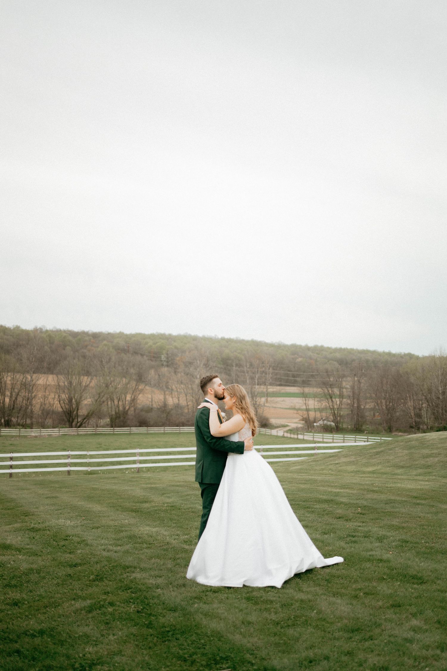 Romantic wedding couple embraces on a sprawling green lawn with rolling hills in the background.