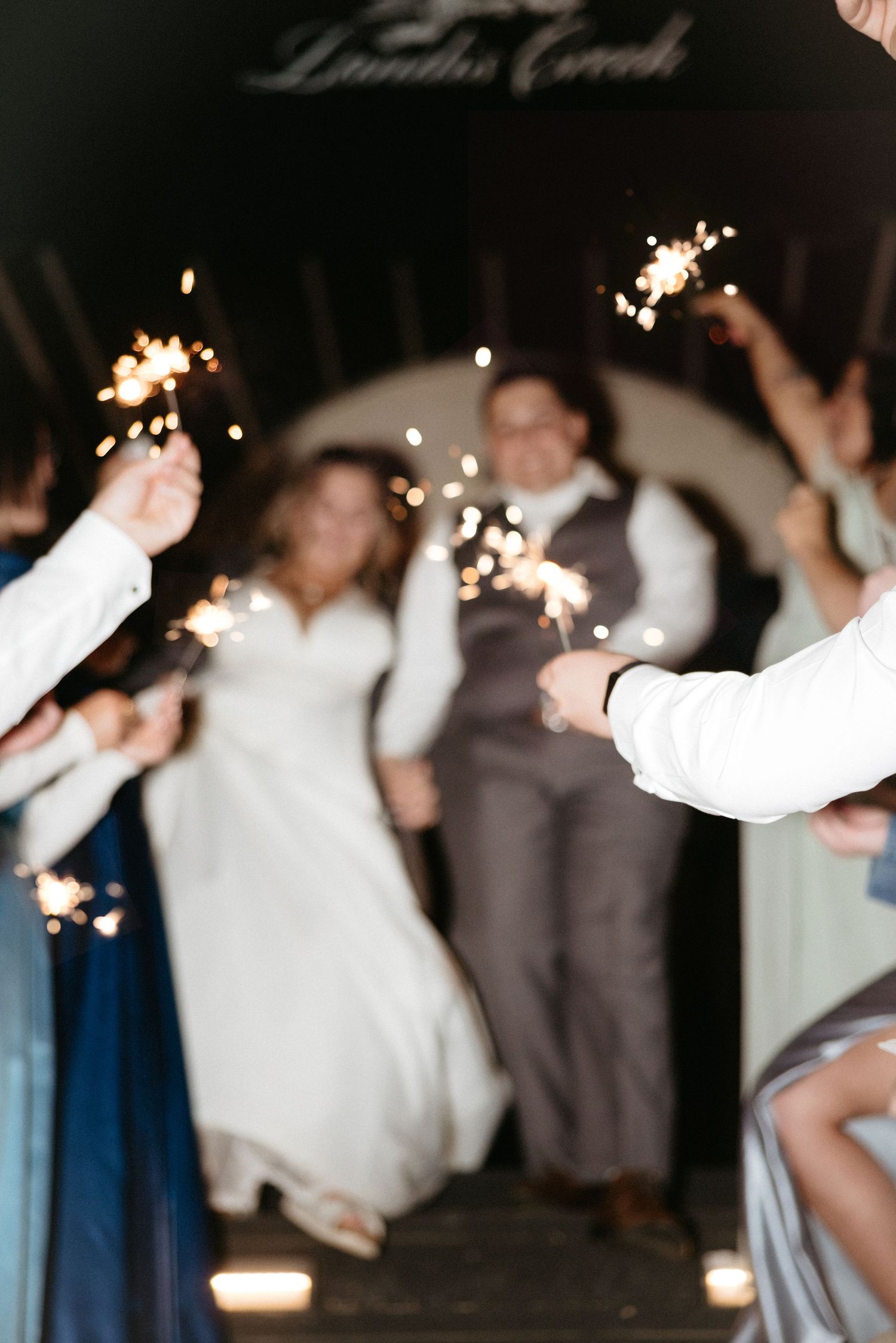 Wedding guests hold sparklers creating a magical exit tunnel with blurred lights and celebratory atmosphere.
