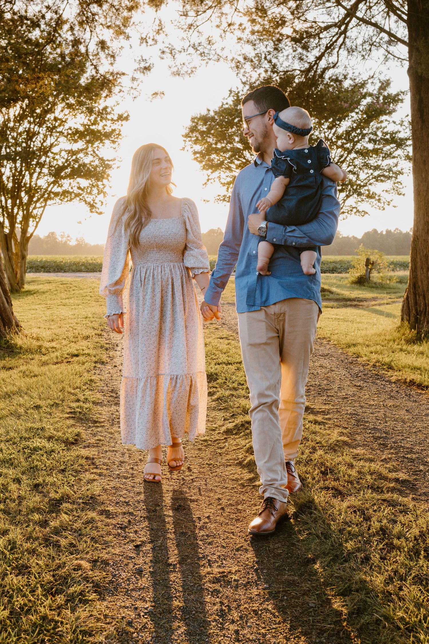 Family on a dirt path at sunset with golden light filtering through trees in a scenic outdoor setting.