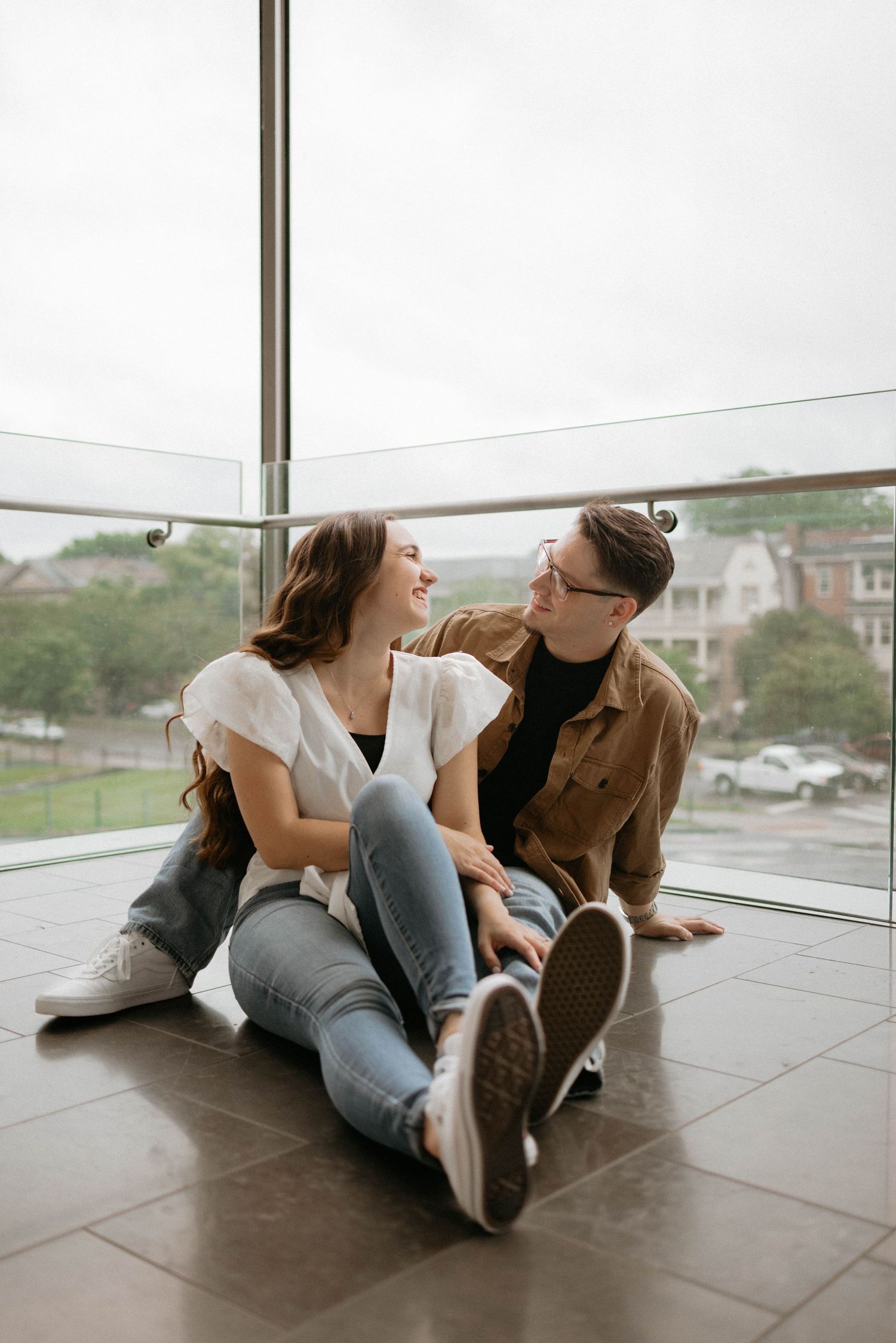 Couple sits together on polished wooden floor while having a playful, lighthearted moment.