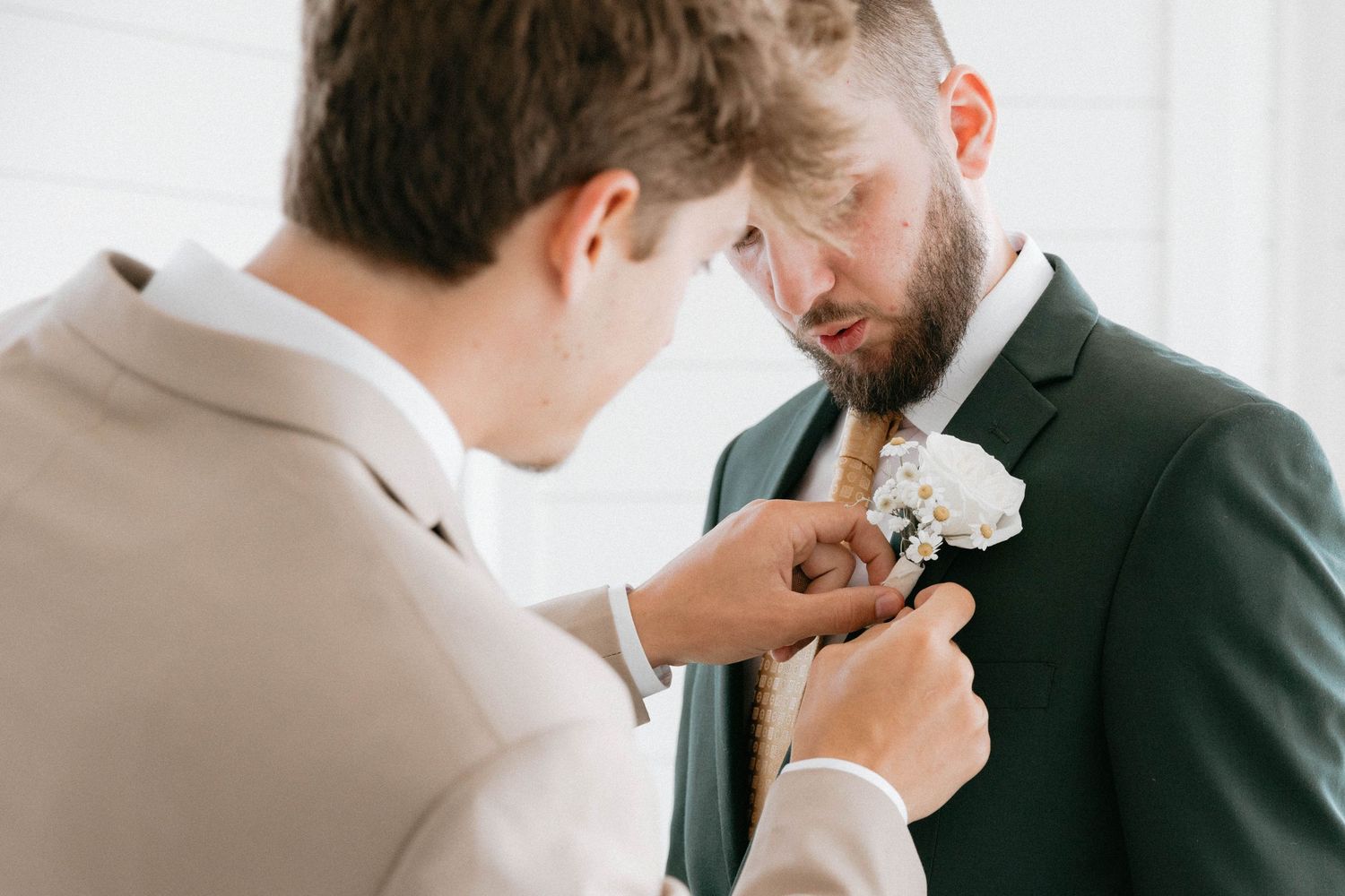 A person in a dark suit helps with boutonniere pinning during a formal wedding occasion.