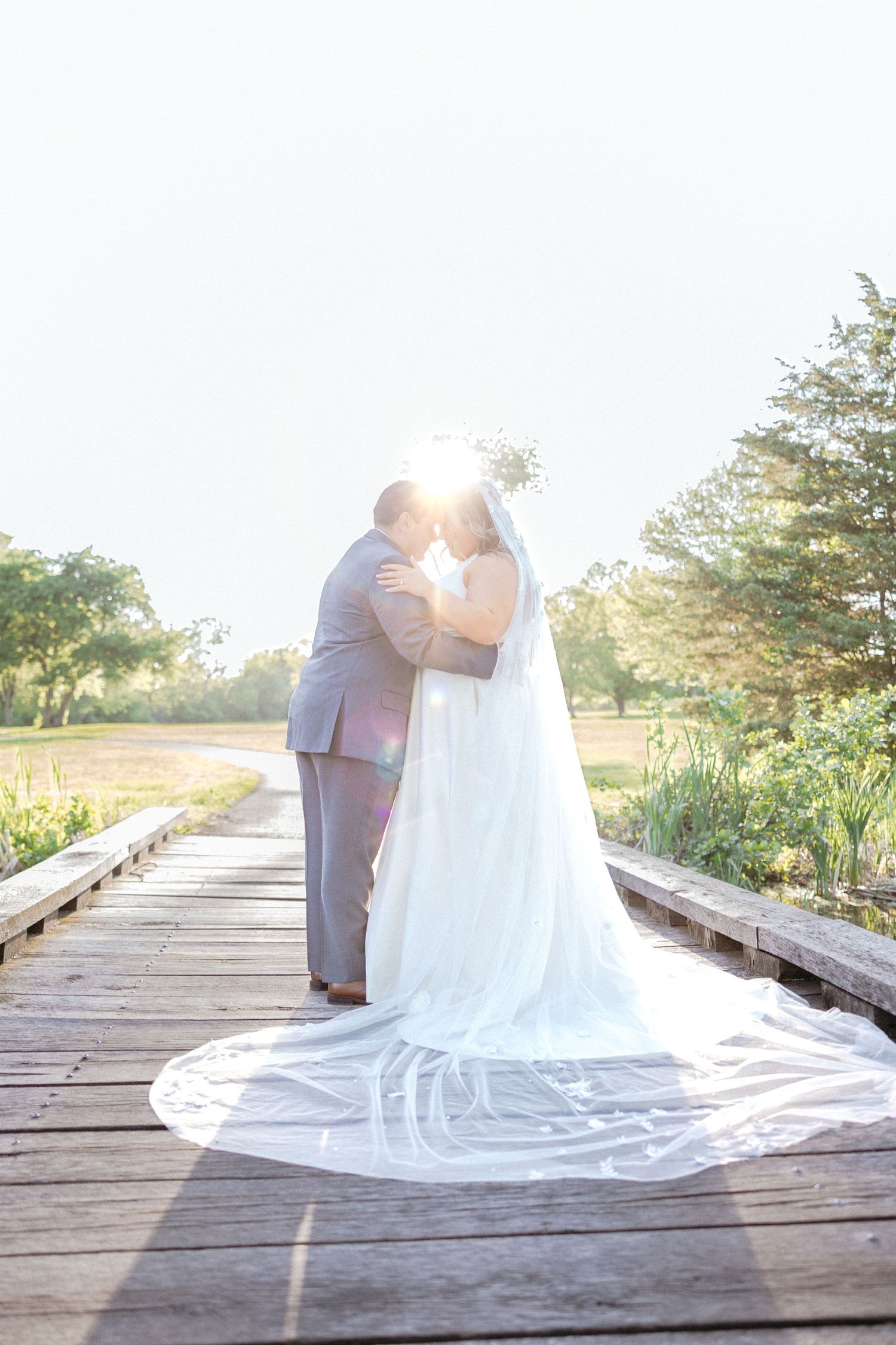 Wedding couple on a wooden boardwalk with flowing white dress train at sunset.
