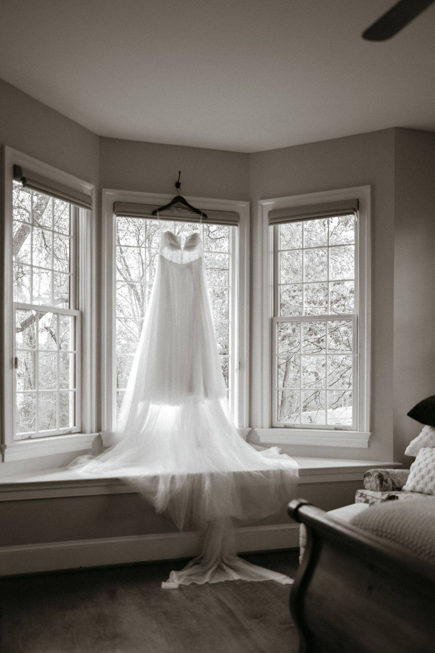 A flowing white wedding veil hangs ethereally near large windows in a light-filled bedroom with neutral tones.