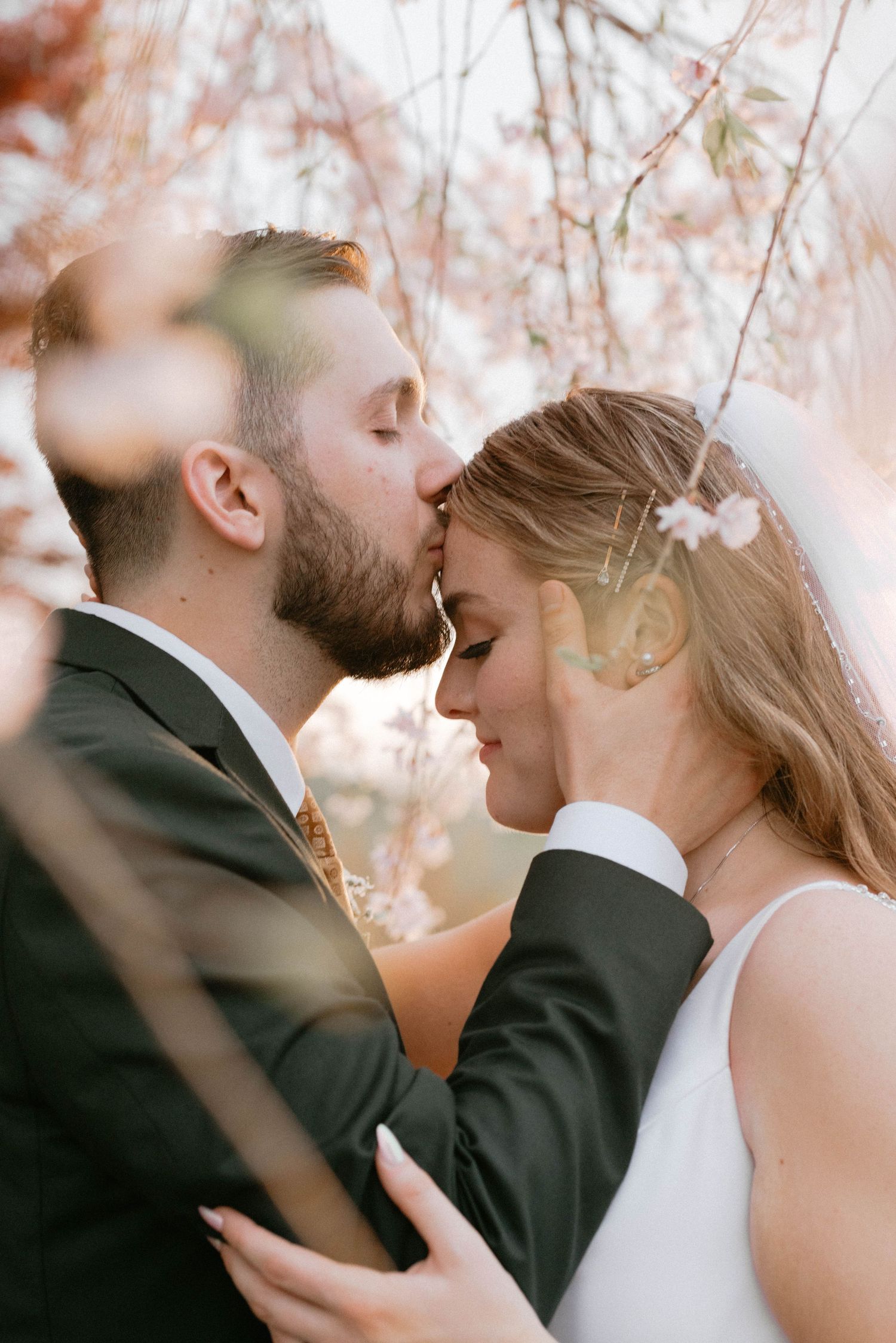Romantic wedding couple sharing intimate moments beneath blooming cherry blossom trees.