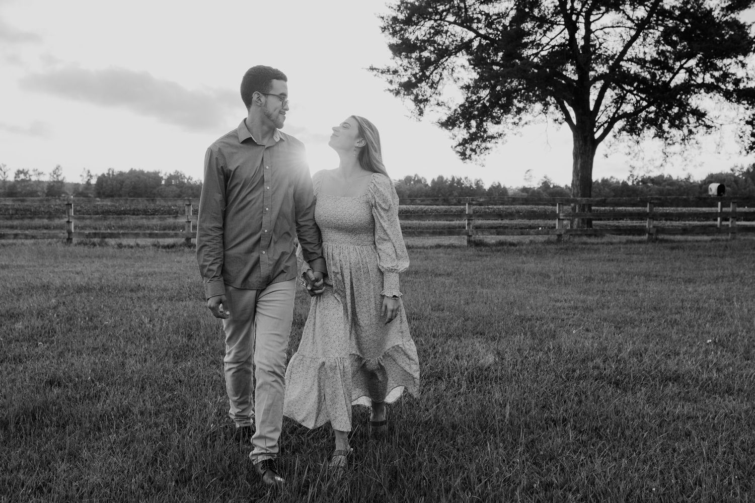 A couple walks together through a scenic countryside field on a sunny afternoon.