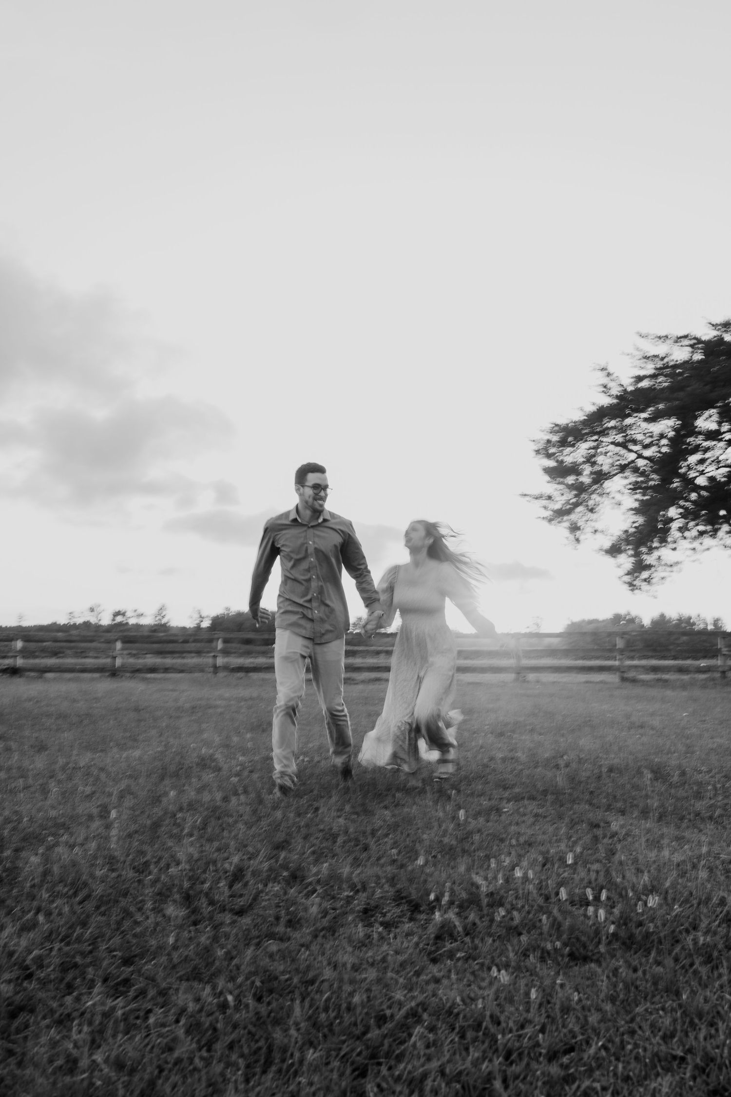 A romantic black and white photo series of a couple walking through a scenic meadow field at sunset.
