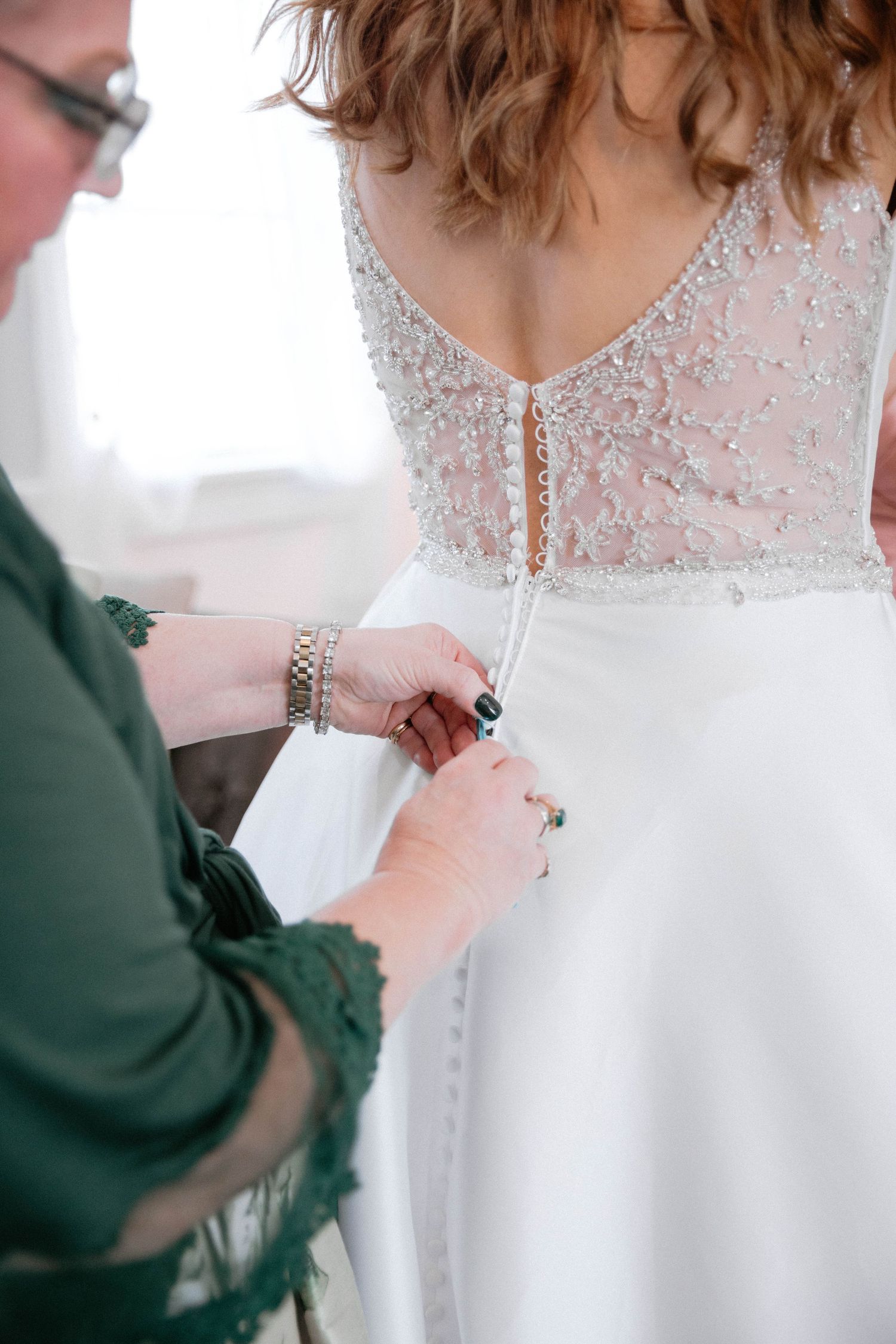 Close-up shots showing the intricate details of buttoning up a delicate white wedding dress with lace details.