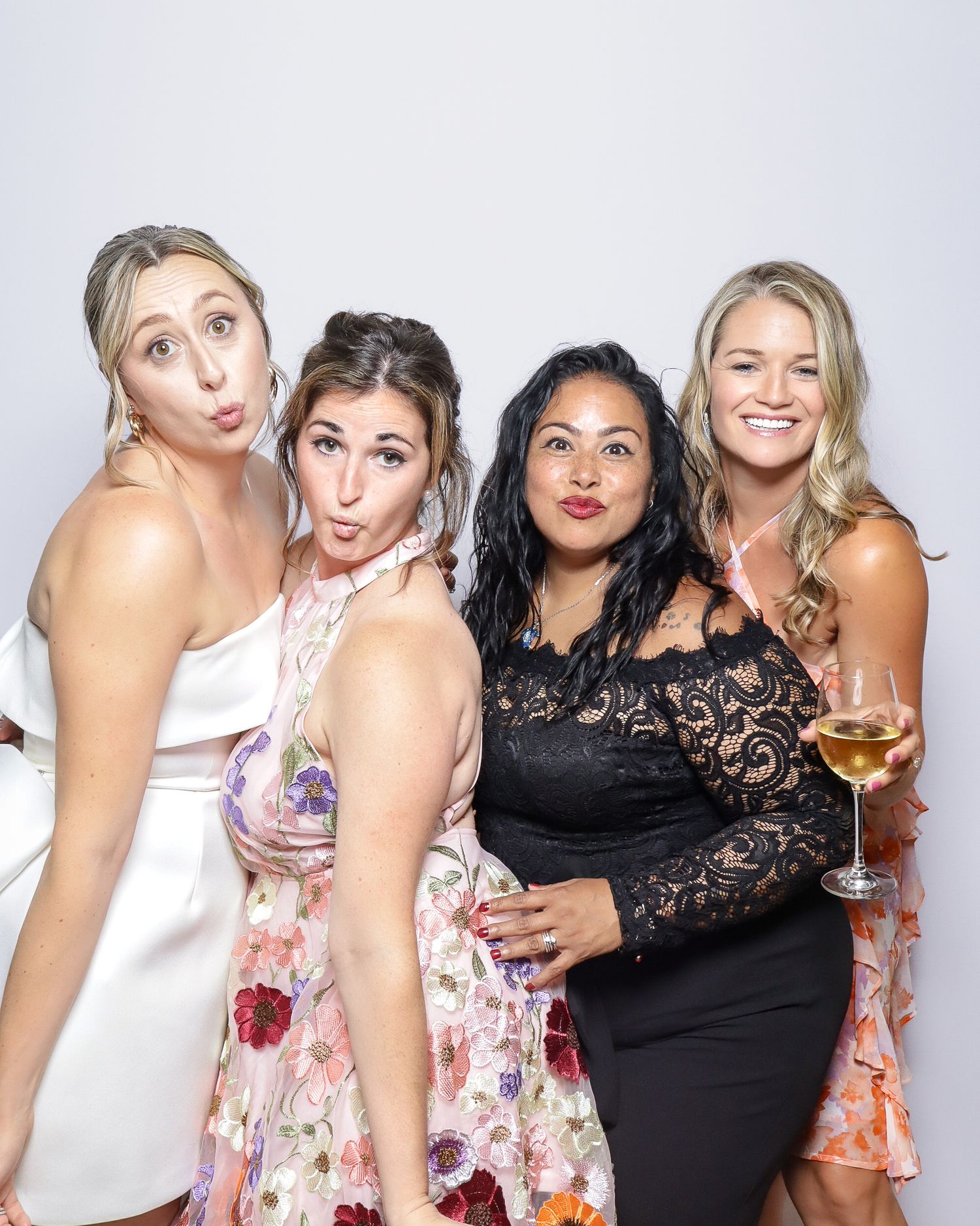 Group of friends pose together with wine glasses at a party photo booth in progressive celebratory shots.