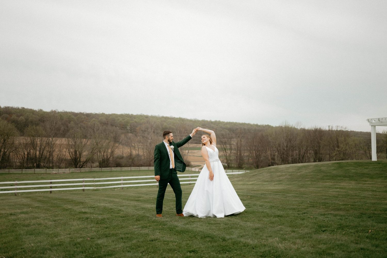 Couple in wedding attire shares a romantic moment in a scenic field at sunset.
