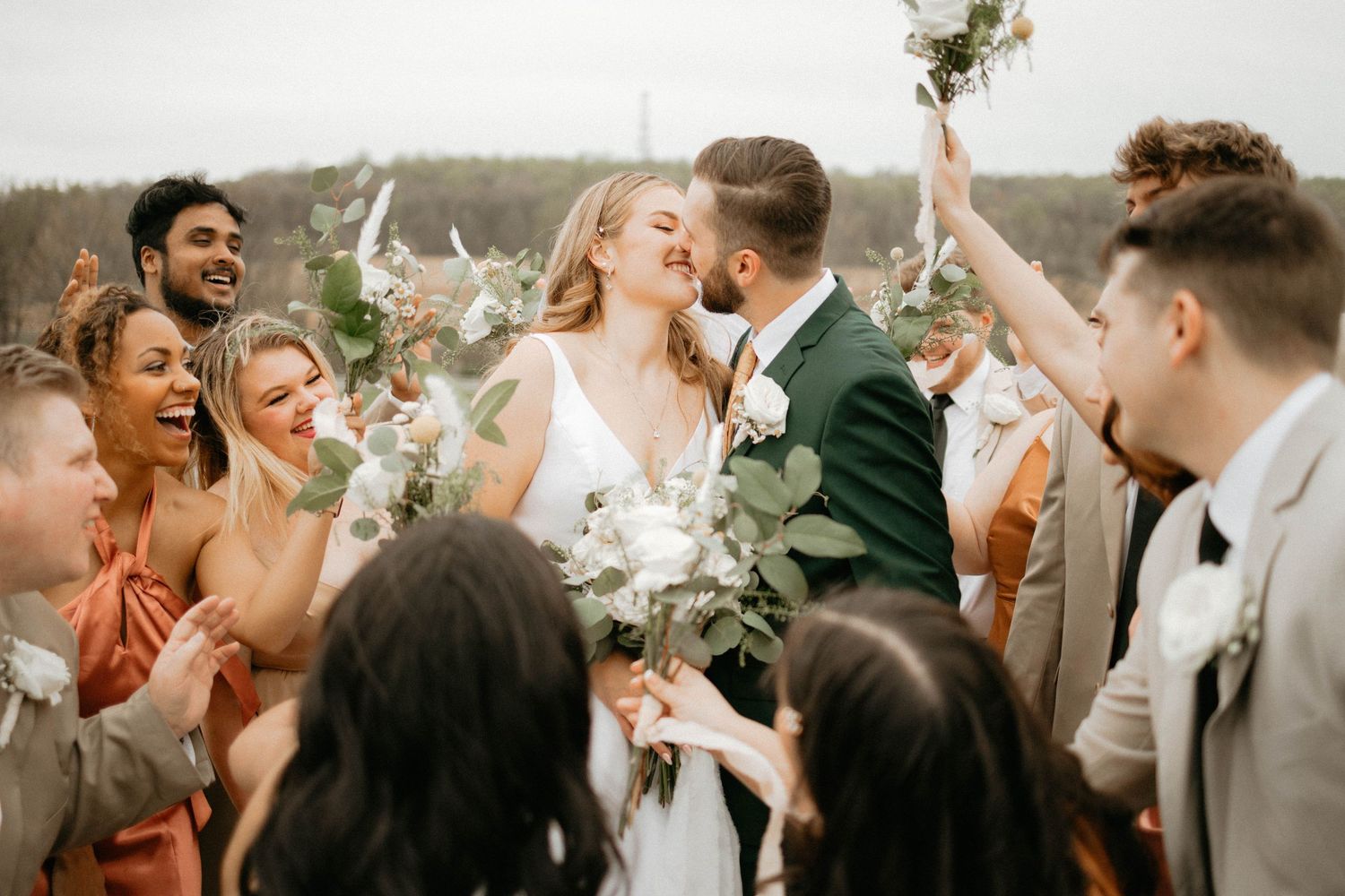 Wedding party celebrating with enthusiastic cheers and raised hands outdoors.