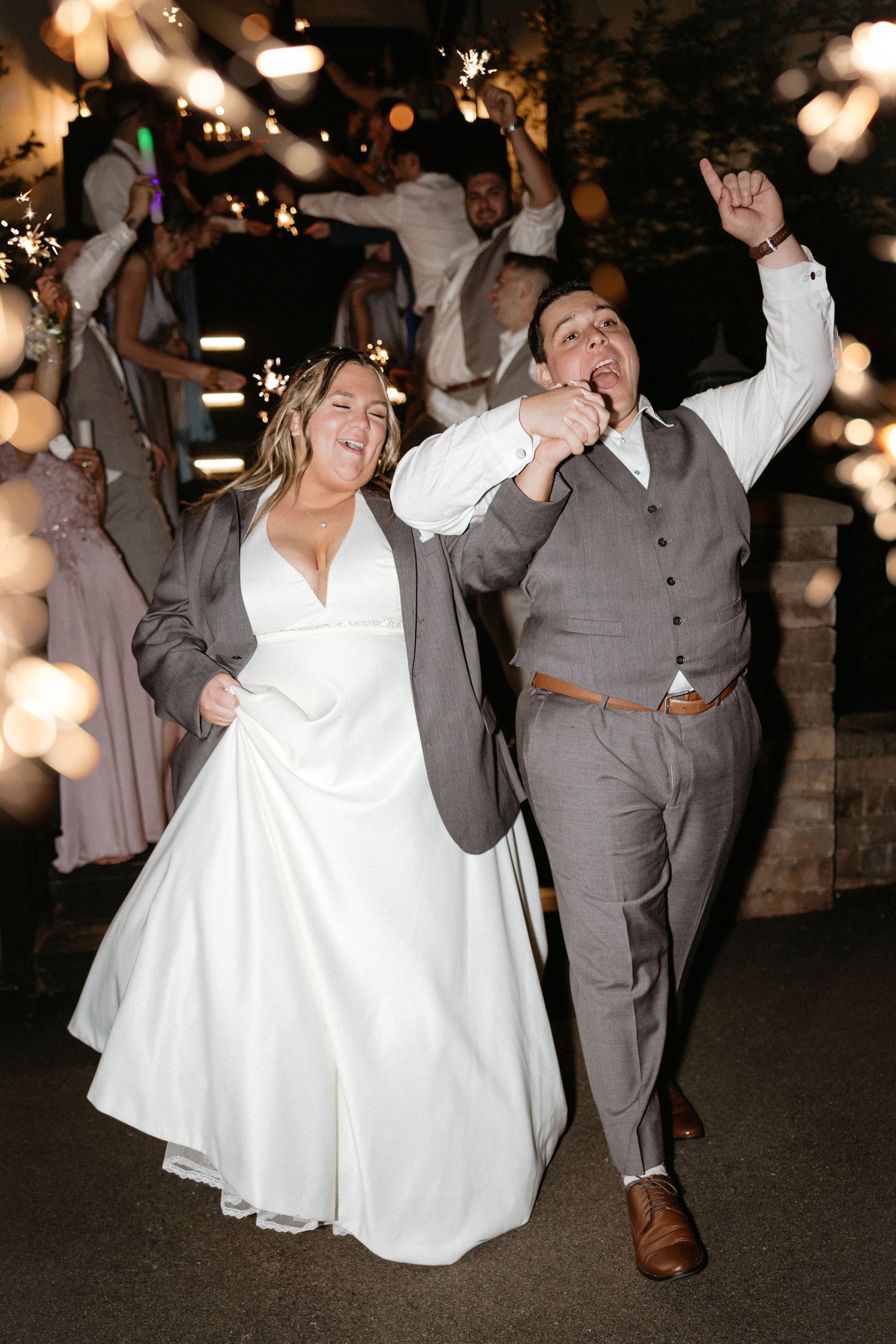 Couple dancing energetically at their wedding reception under string lights at night.