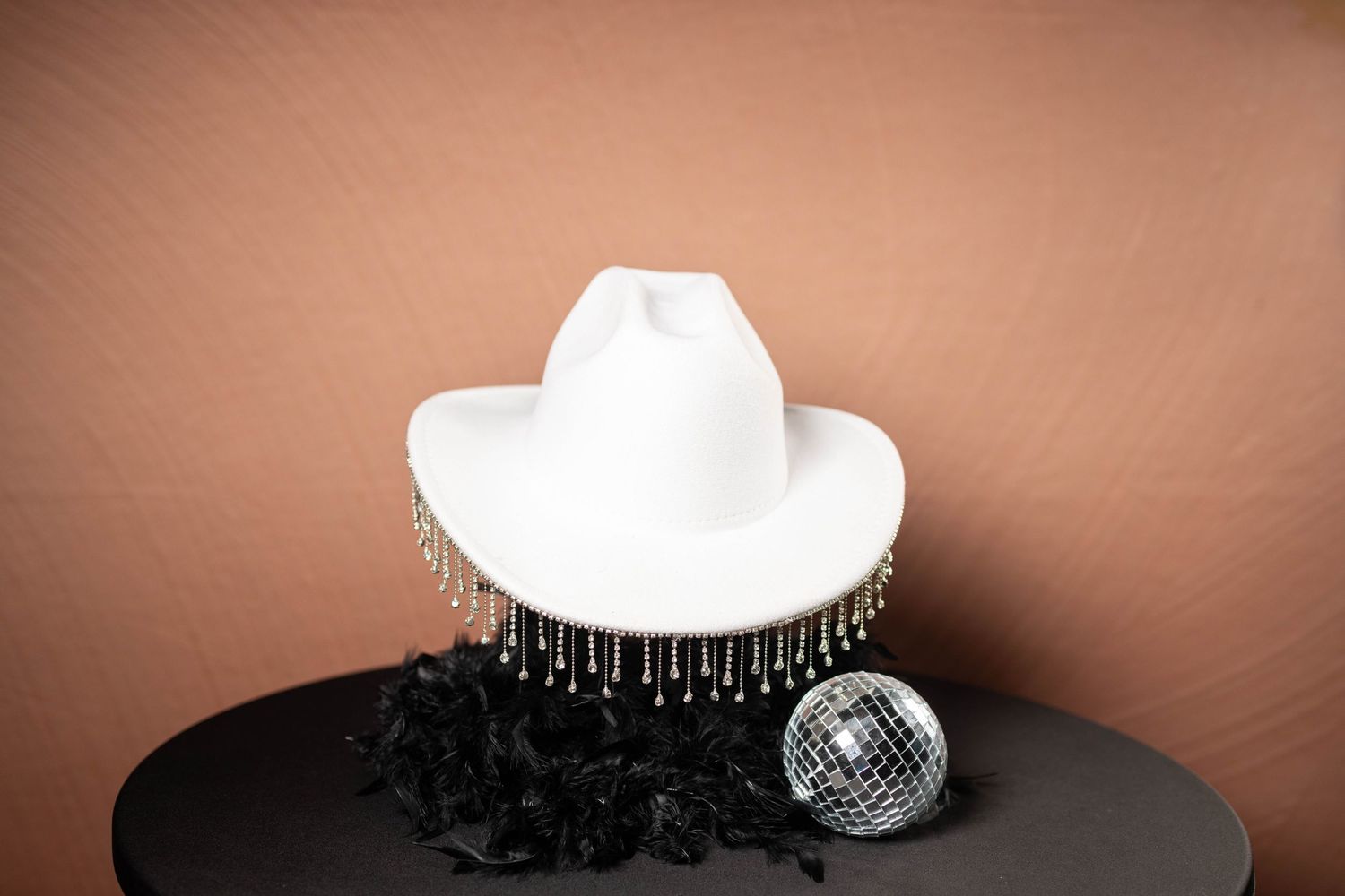 Collection of fashion accessories arranged with a white column and disco ball on brown surface.