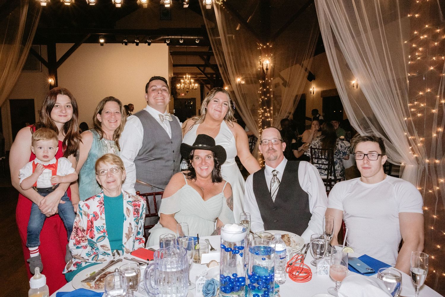 Wedding reception guests enjoying dinner at tables decorated with festive lighting and white linens.